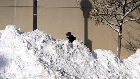A man walks past mounds of plowed snow from nine consecutive days of measurable and fresh fallen snow Tuesday, Feb. 16, 2021, in Chicago. (AP Photo/Charles Rex Arbogast)