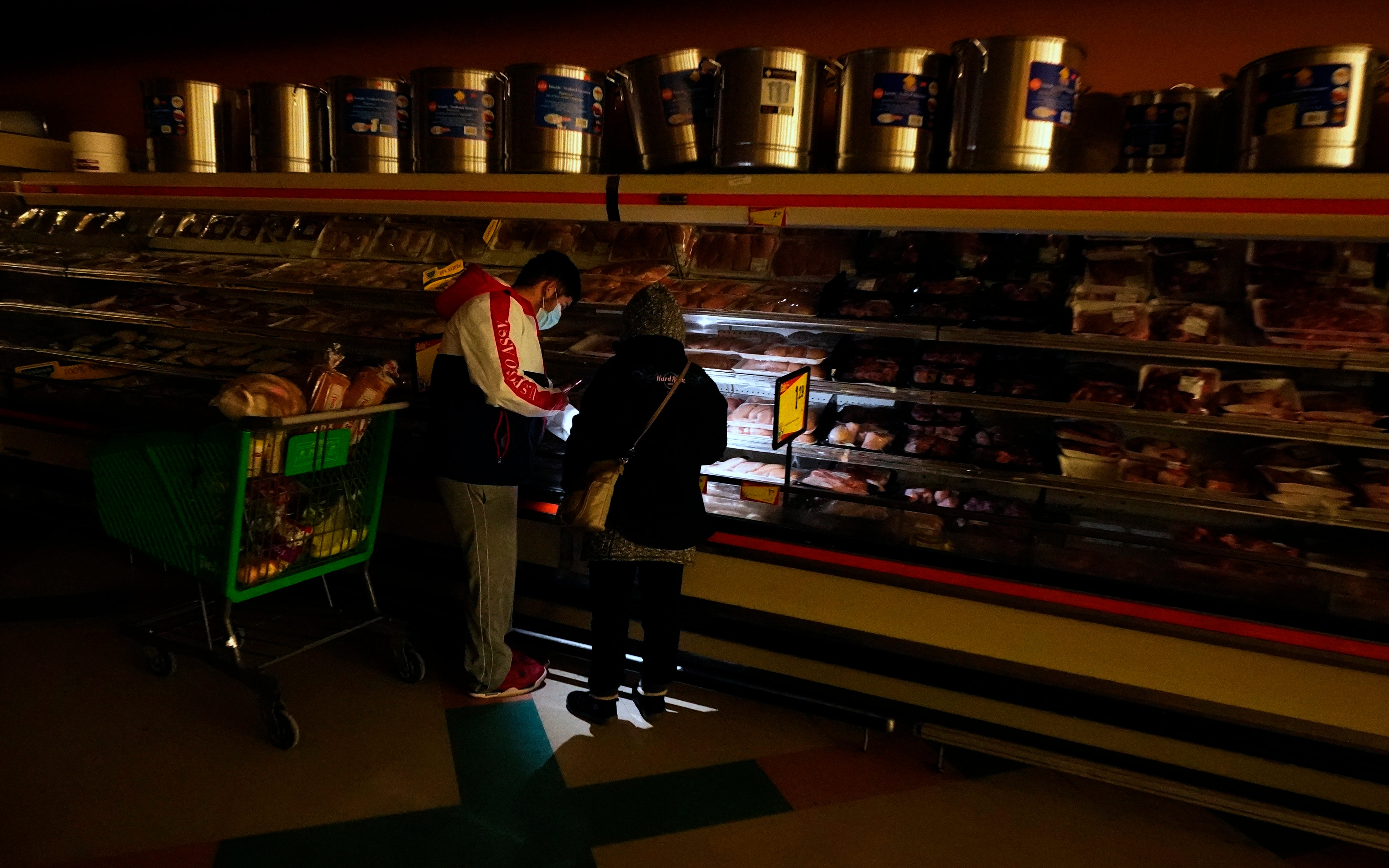 Customers use the light from a cell phone to look in the meat section of a grocery store Tuesday, Feb. 16, 2021, in Dallas. Even though the store lost power, it was open for cash only sales. (AP Photo/LM Otero)
