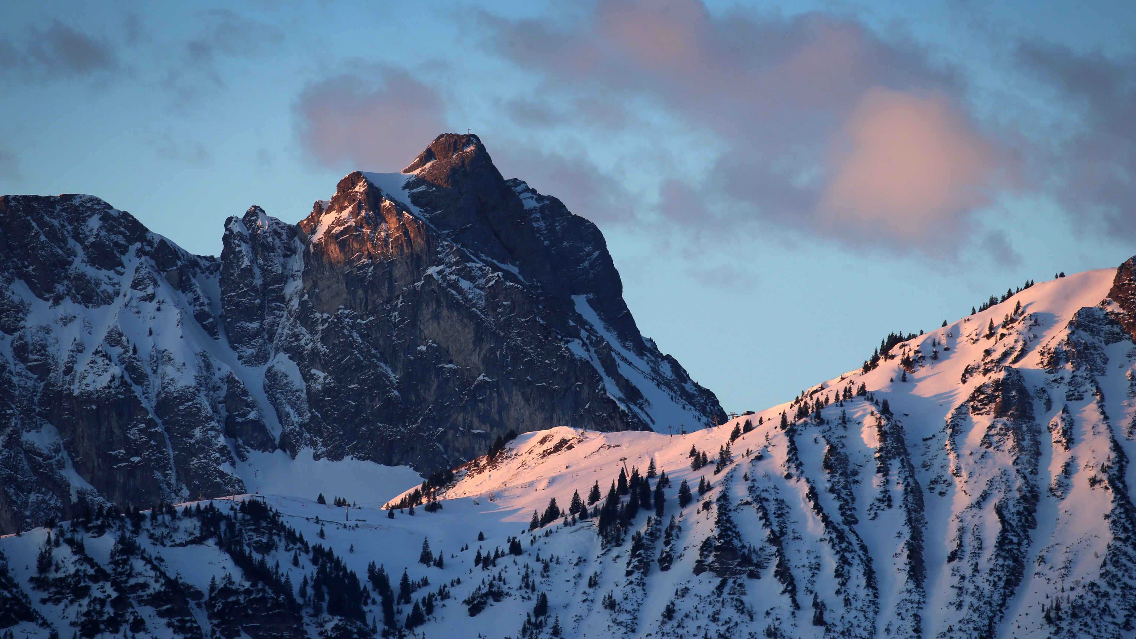 Pfronten: Der Gipfel des Aggensteins und der Schnee auf den Skipisten des Breitenbergs leuchten im Licht der aufgehenden Sonne r&ouml;tlich.