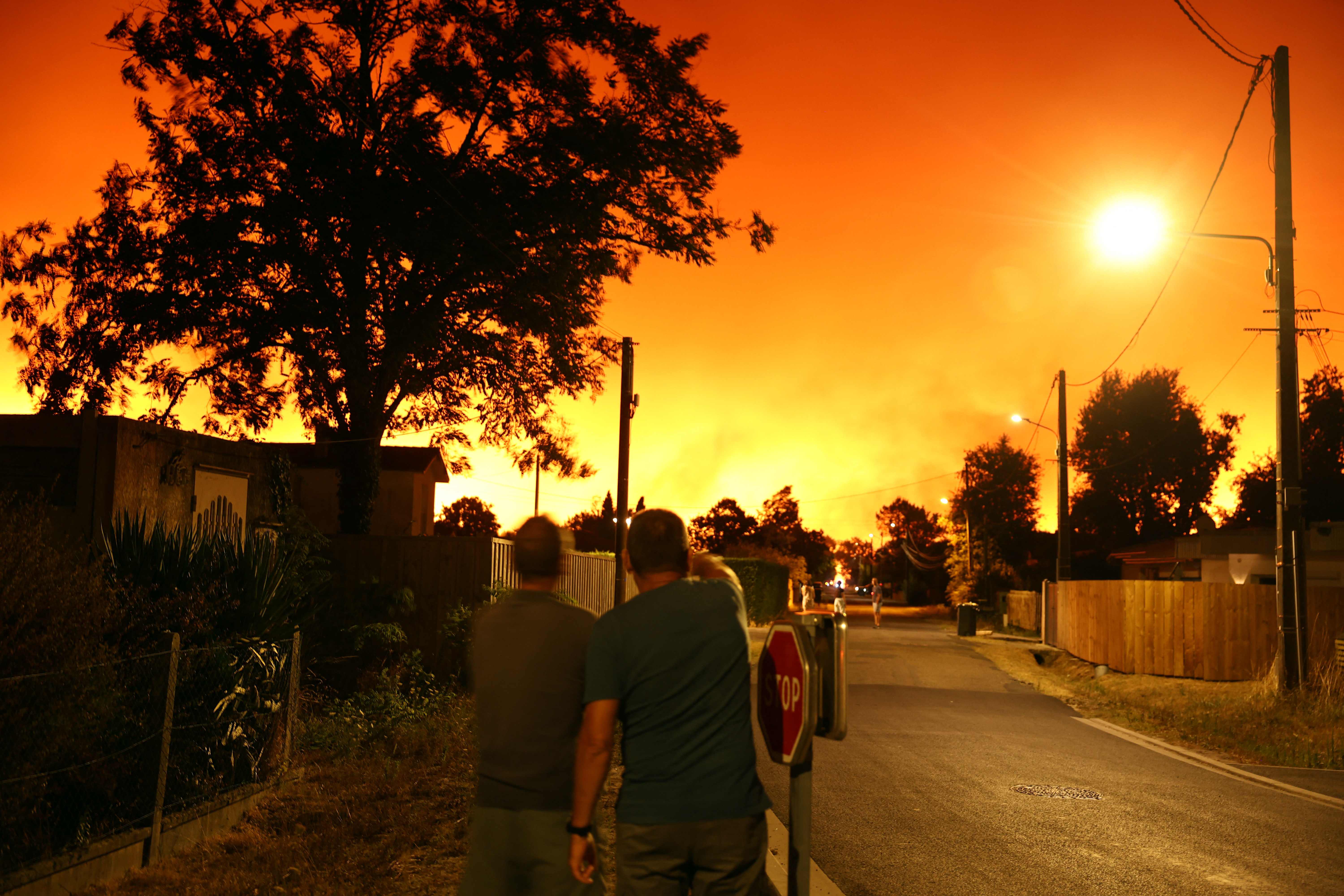 23.07.2026, Frankreich, Le Porge: Anwohner blicken am fr&uuml;hen Morgen in Le Porge im S&uuml;dwesten Frankreichs in den von Waldbr&auml;nden erhellten Himmel. (Romain Perrocheau/AFP/dpa)

