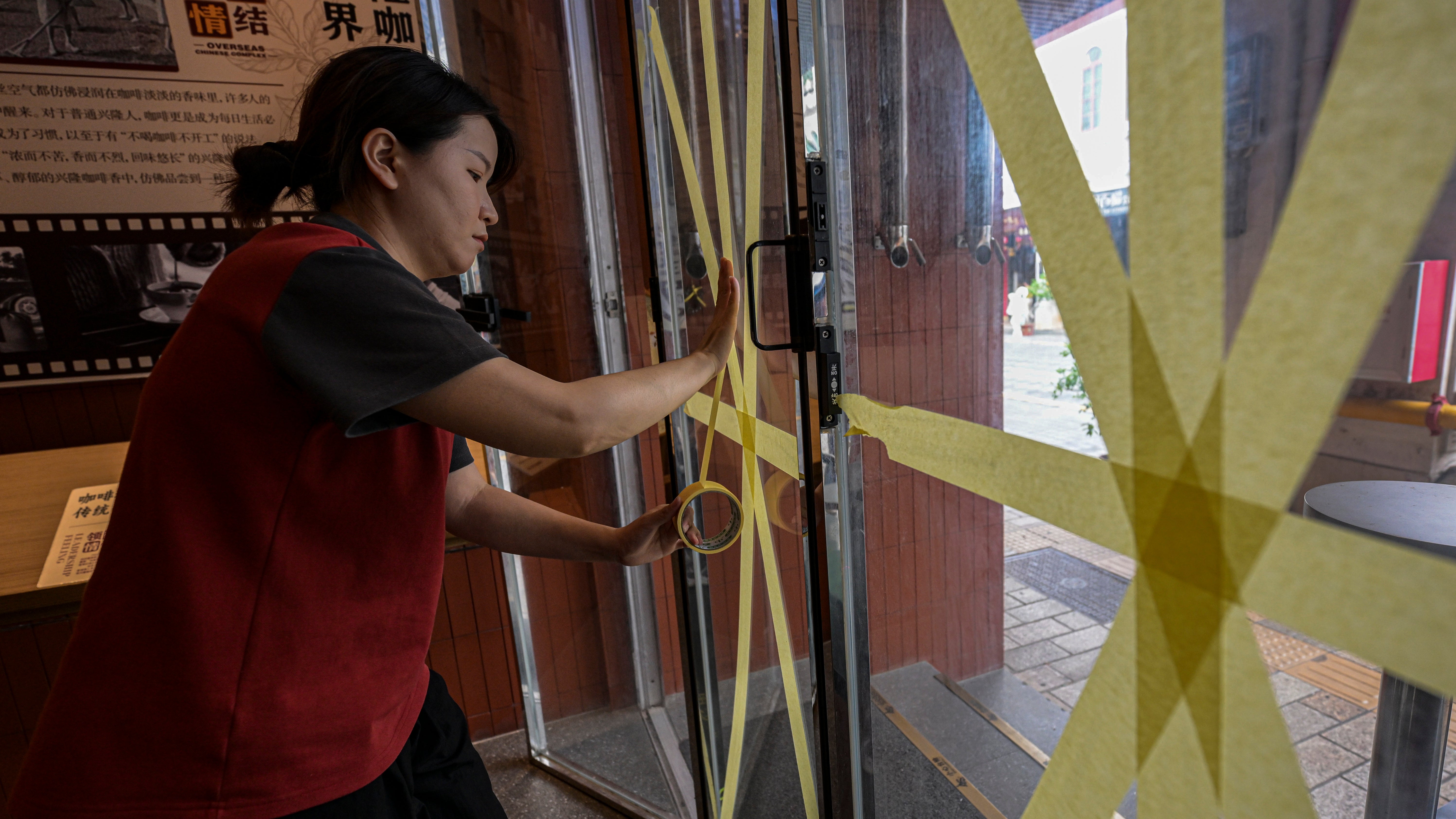 5. September 2024, in Haikou: Auf diesem von der Nachrichtenagentur Xinhua ver&ouml;ffentlichten Bild verst&auml;rkt eine Frau vor der Ankunft von Taifun Yagi ein Glasfenster in einem Caf&eacute; mit Klebeband. (Pu Xiaoxu/Xinhua via AP)