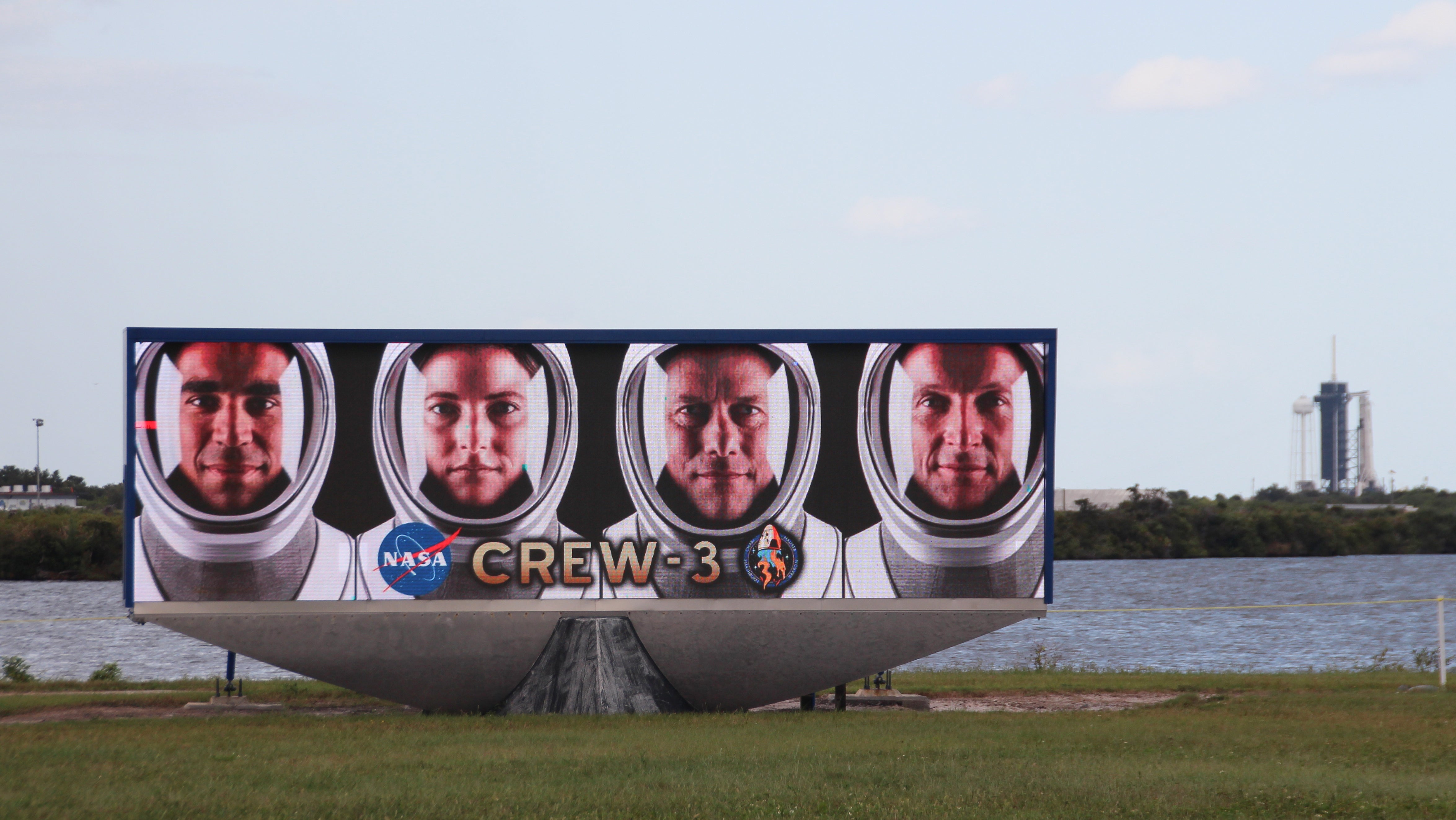 Cape Canaveral: Ein Video-Bildschirm zeigt die Gesichter der vier Astronauten der Crew-3 (l-r): Raja Chari, Kayla Barron, Thomas Marshburn und Matthias Maurer vor dem Launchpad 39A, an dem schon die Falcon-9-Rakete mit Crew Dragon-Kapsel aufgestellt ist.