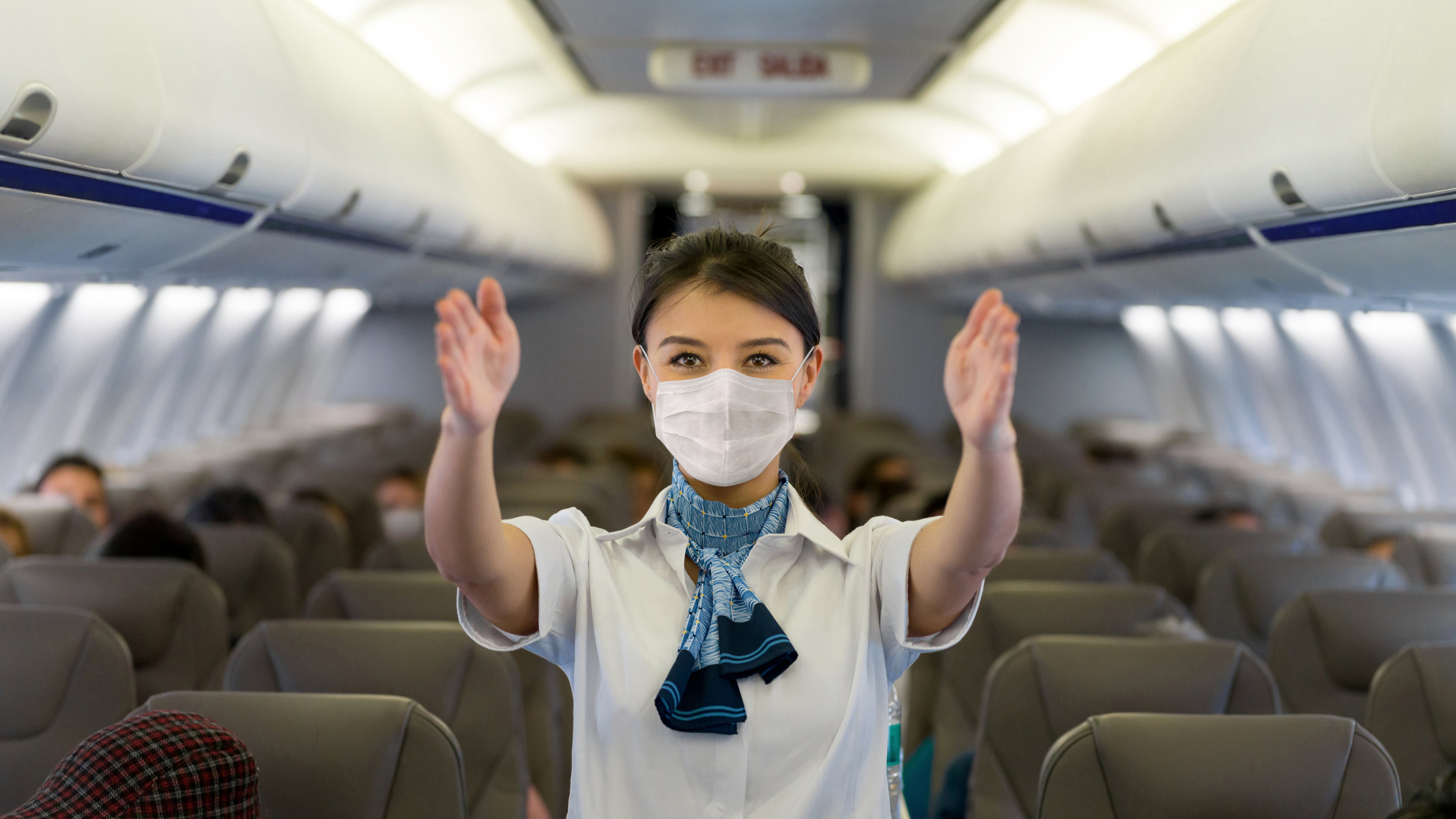 Eine Stewardess mit Maske gibt an Bord eines Flugzeuges Sicherheitsanweisungen