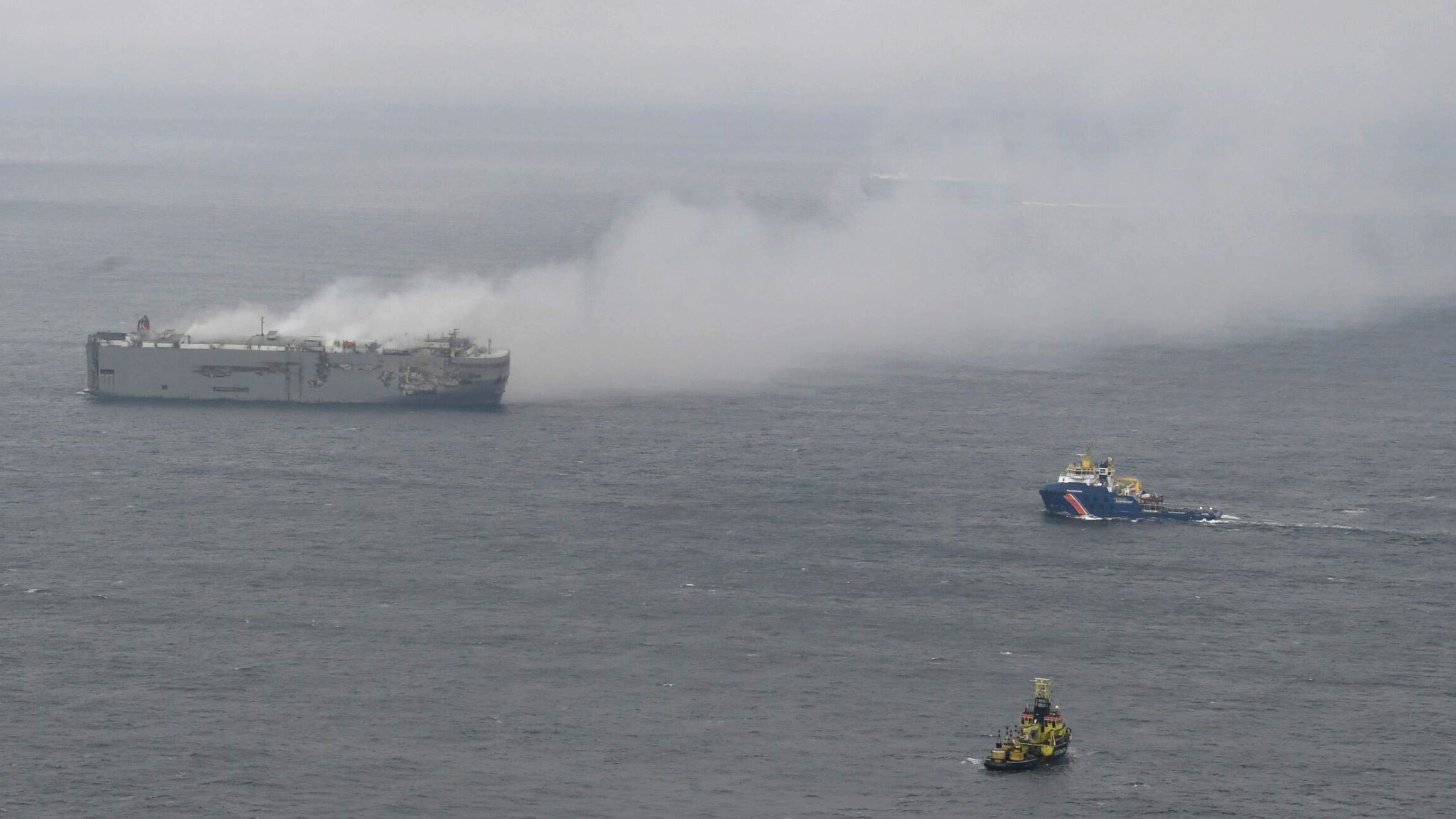 dpatopbilder - HANDOUT - 27.07.2023, Niederlande, Nordsee: Ein Foto, das aus einem Flugzeug der niederl&auml;ndischen K&uuml;stenwache aufgenommen wurde, zeigt dicke Rauchwolken &uuml;ber dem Autofrachter "Fremantle Highway" in der Nordsee, der umgeben ist von Schleppern. Foto: Coast Guard Netherlands/dpa - ACHTUNG: Nur zur redaktionellen Verwendung im Zusammenhang mit der aktuellen Berichterstattung und nur mit vollst&auml;ndiger Nennung des vorstehenden Credits +++ dpa-Bildfunk +++