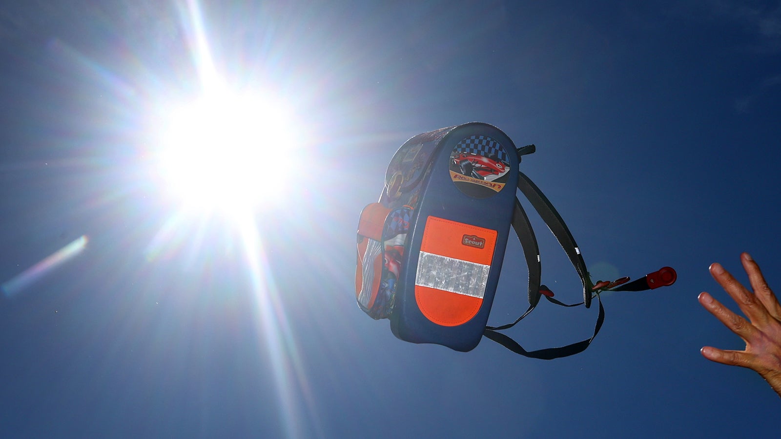 ILLUSTRATION - 03.07.2022, Bayern, Kaufbeuren: Eine B&uuml;chertasche wird vor dem sonnigen Himmel hochgeworfen. Anspruch auf Hitzefrei hat kein Kind. Die heutigen Regelungen dazu sind von Bundesland zu Bundesland unterschiedlich.     (zu dpa "Fr&uuml;her gab's Hitzefrei - heute meist Aufsichtspflicht statt Badesee") Foto: Karl-Josef Hildenbrand/dpa +++ dpa-Bildfunk +++