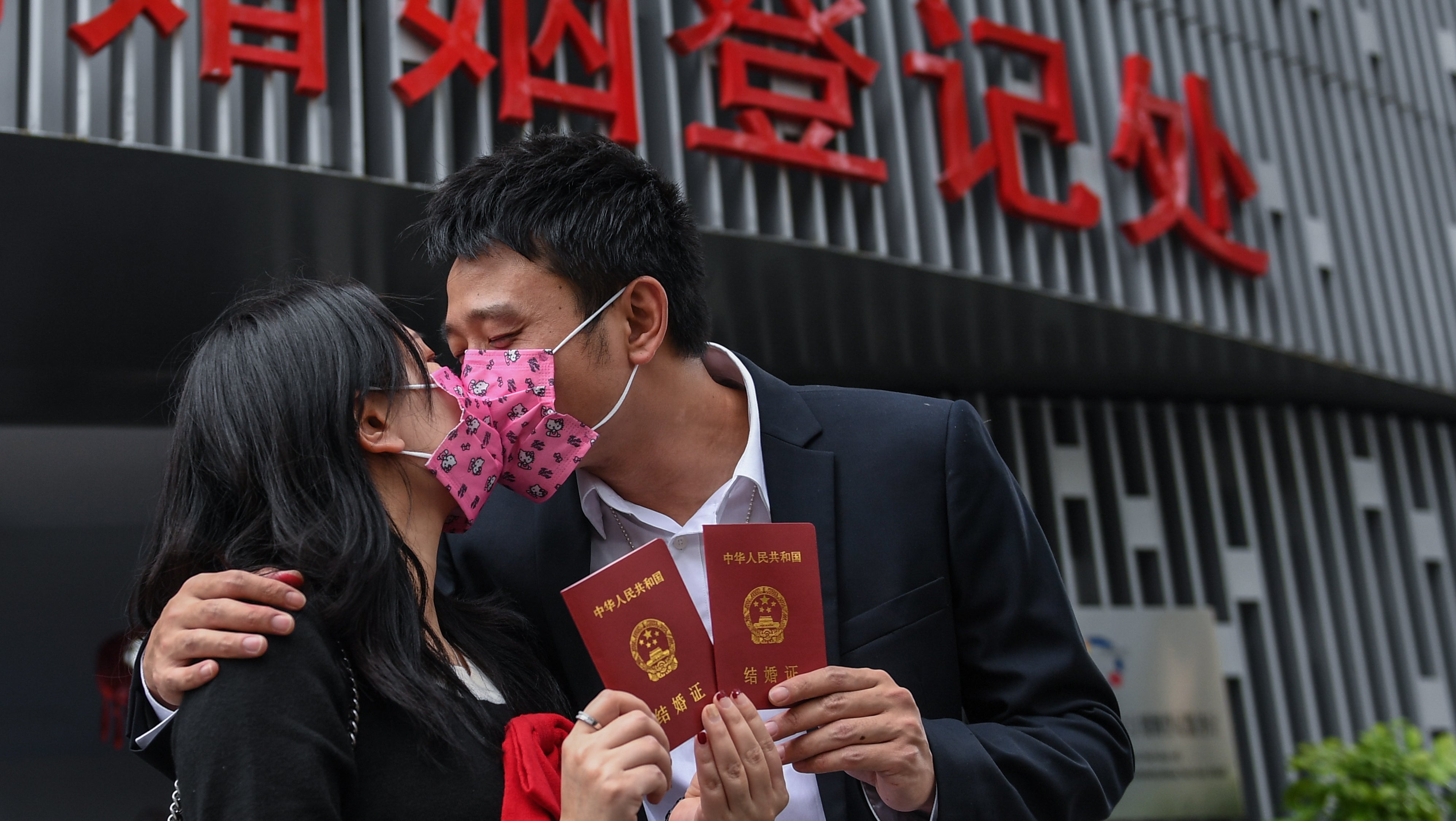 China, Shenzhen: Deng Lingling (l) und Deng Junwei tragen Mundschutz und k&uuml;ssen sich, w&auml;hrend sie ihre Heiratsurkunden vor dem Standesamt des B&uuml;ros f&uuml;r Zivile Angelegenheiten des Bezirks Nanshan in Chinas Provinz Guangdong halten.