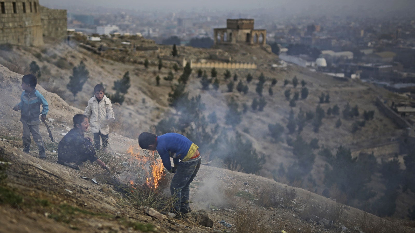 26.11.2019, Afghanistan, Kabul: Afghanische Kinder machen ein Lagerfeuer auf einem H&uuml;gel mit Blick auf das Grab von Nadir Shah. Foto: Altaf Qadri/AP/dpa +++ dpa-Bildfunk +++
