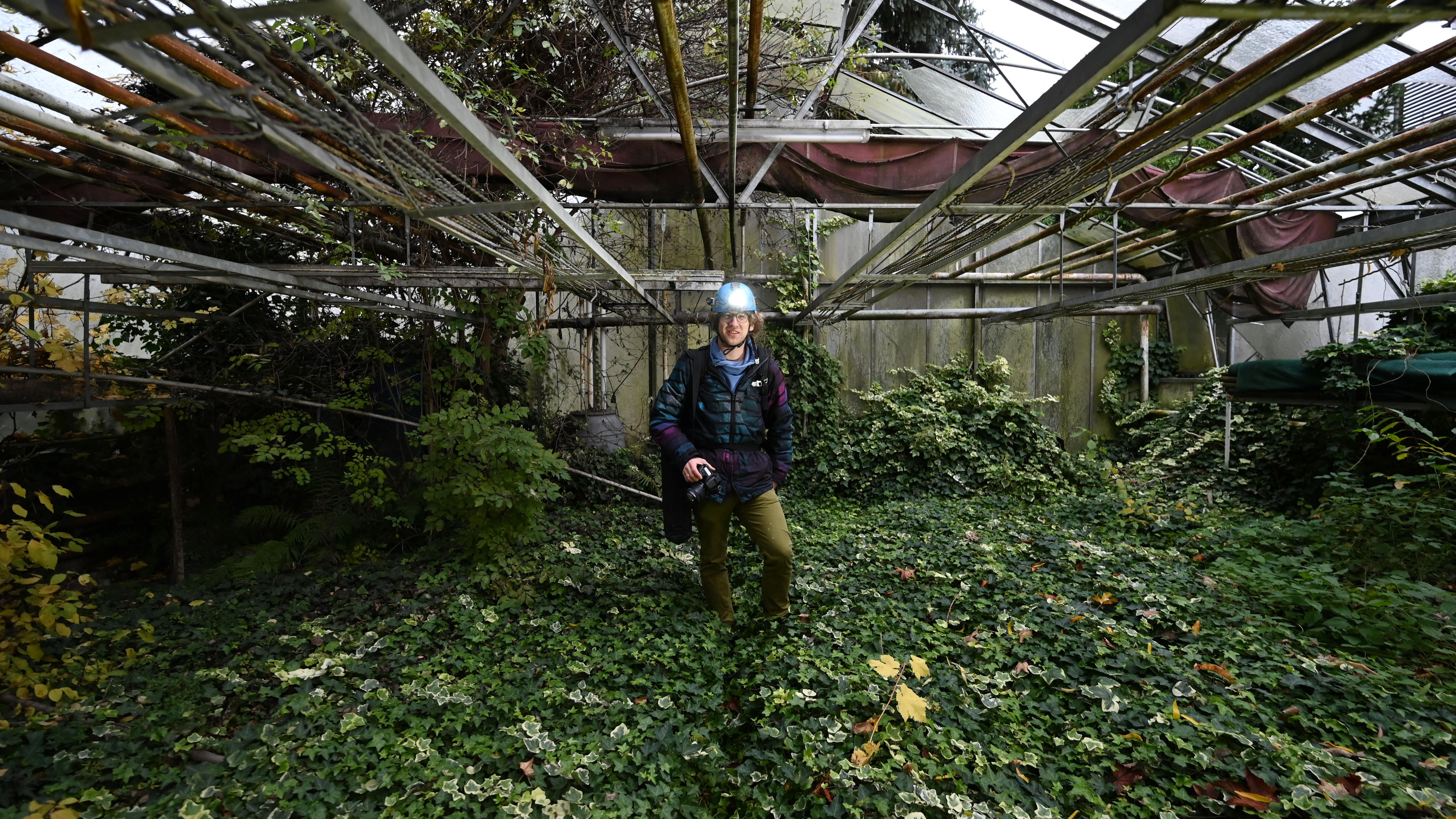 Benjamin Seyfang steht in einem verfallenen Gew&auml;chshaus einer ehemaligen G&auml;rtnerei.