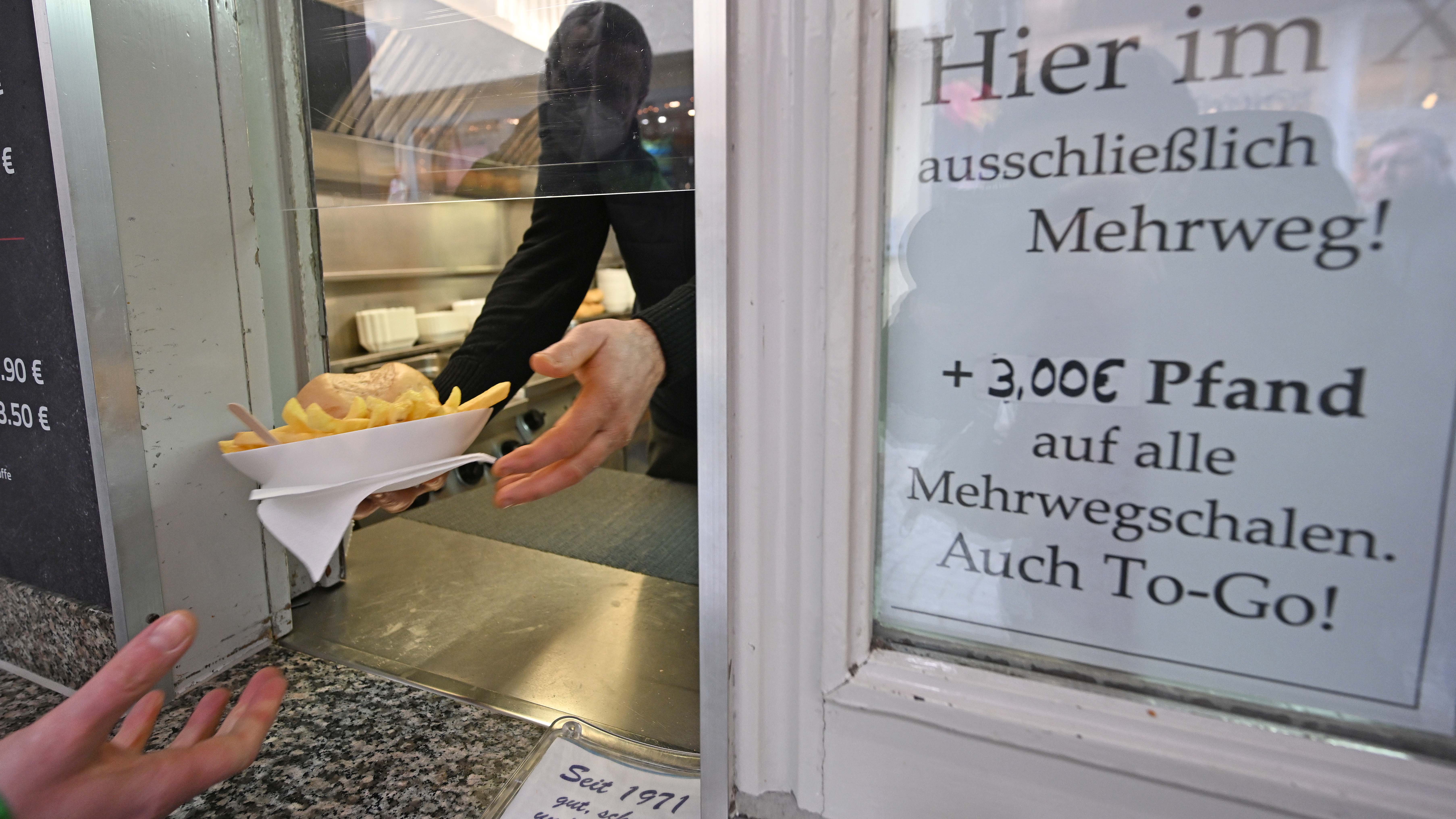 ARCHIV - 28.01.2021, Baden-W&cedil;rttemberg, T&cedil;bingen: Eine Hand h&permil;lt an einem Imbiss in der Innenstadt einen Mehrwegteller mit Pommes und einem Burger. Kunden haben k&cedil;nftig ein Anrecht darauf, ihre To-Go-Speisen und -Getr&permil;nke in einer Mehrwegverpackung zu bekommen. (zu dpa: "Essen und Trinken to go: ab Januar auch in Mehrwegverpackungen") Foto: Bernd Weiﬂbrod/dpa +++ dpa-Bildfunk +++