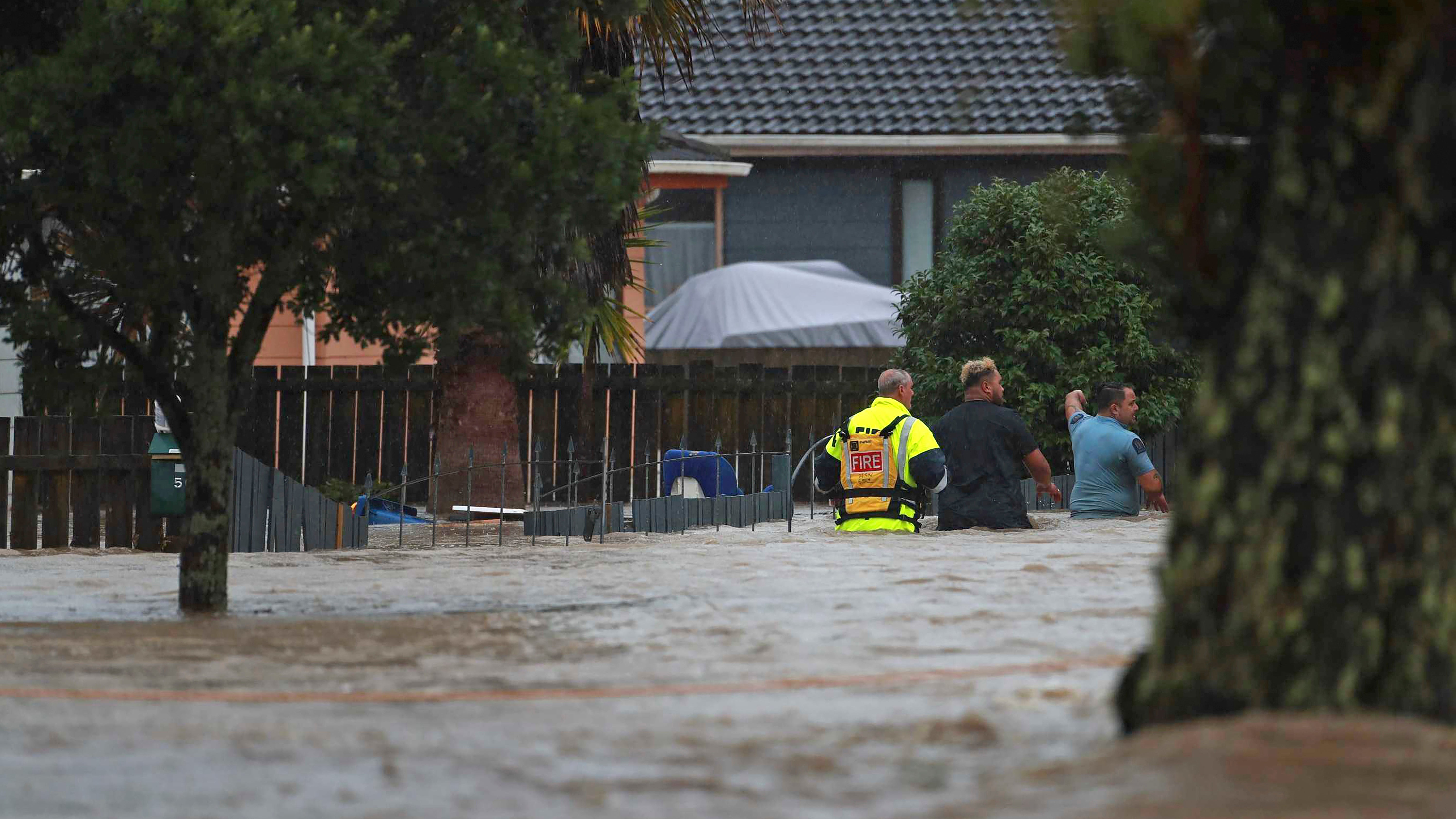 26.01.2023, Neuseeland, Auckland: Rettungskr&auml;fte und ein Mann waten durch das Hochwasser einer &uuml;berschwemmter Stra&szlig;e. Nach massiven Regenf&auml;llen stehen weite Teile Aucklands unter Wasser. Die B&uuml;rger der Metropole wurden vom Zivilschutz aufgefordert, sich in Sicherheit zu bringen. Foto: Hayden Woodward/New Zealand Herald/AP/dpa +++ dpa-Bildfunk +++