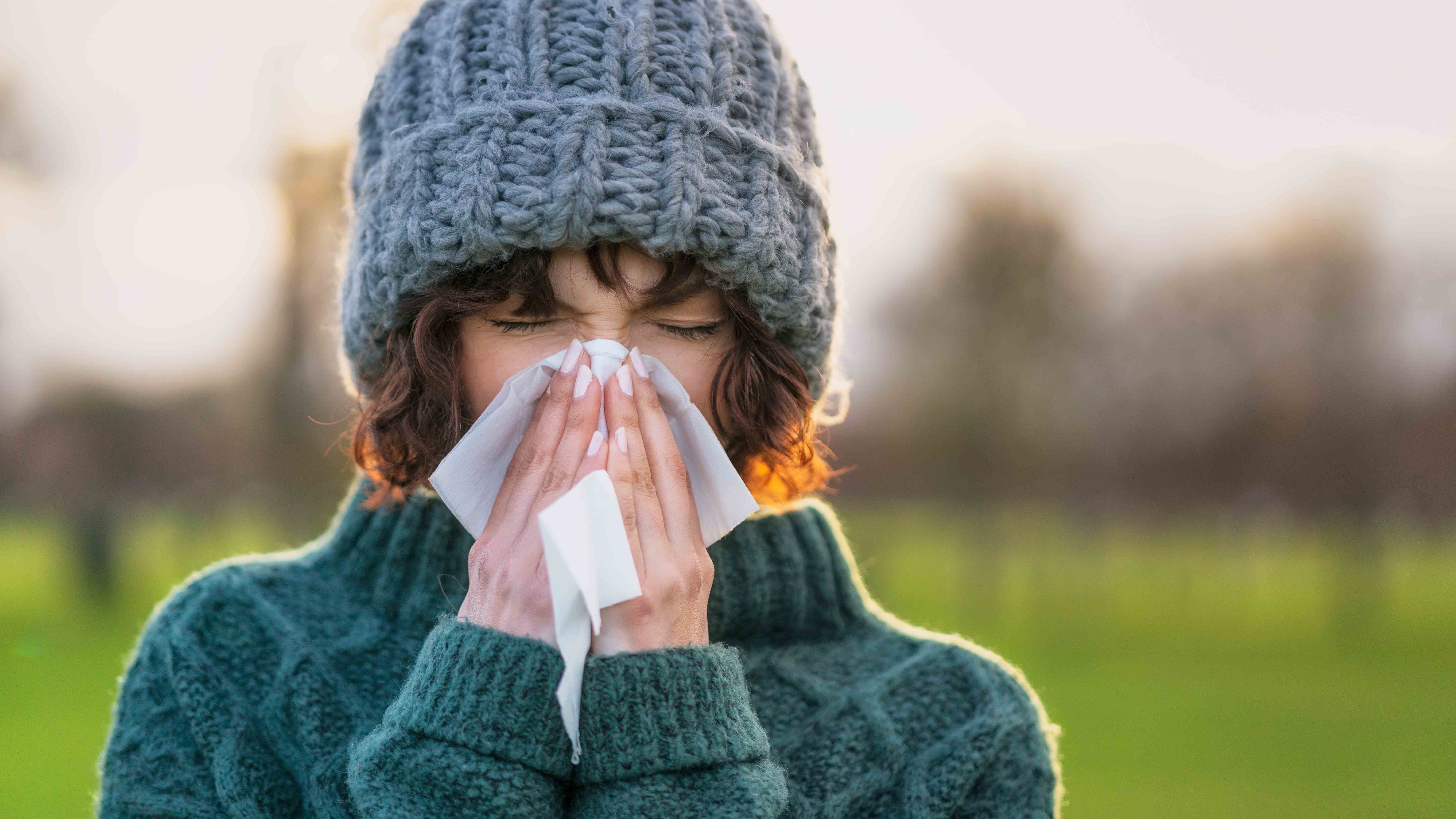 Close-up of a woman suffering from the symptoms of a cold outdoors during winter.