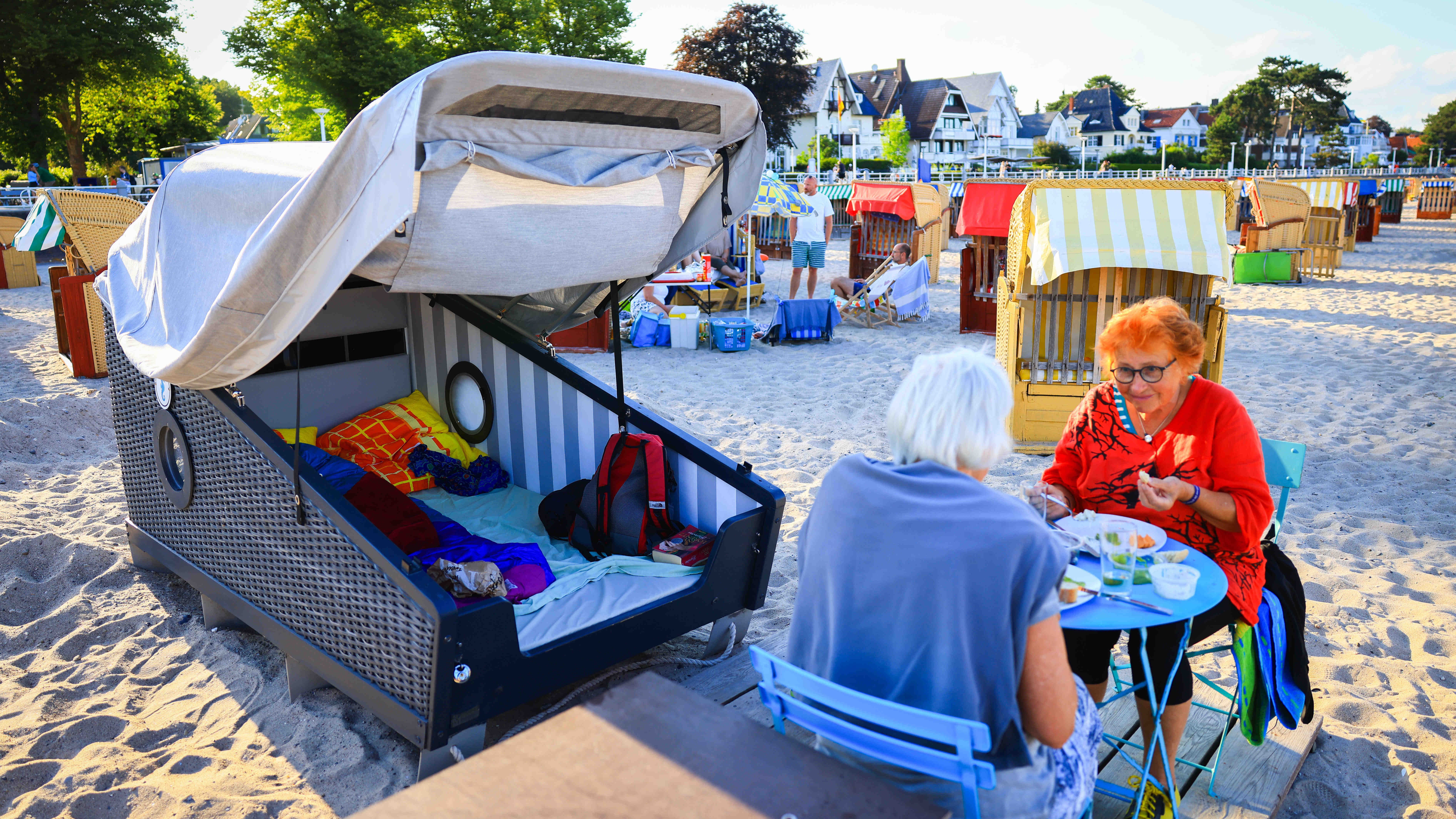 14.07.2022, Schleswig-Holstein, Travem&uuml;nde: Wiltrud Sadlowski (r) und Marion Schleevoight sitzen im Sonnenuntergang beim Abendbrot vor ihrem gemieteten Schlafstrandkorb an der Ostsee. Das &Uuml;bernachten am Strand mit Meeresrauschen im Ohr und dem Sternenhimmel im Blick wird immer beliebter. (Christian Charisius/dpa)