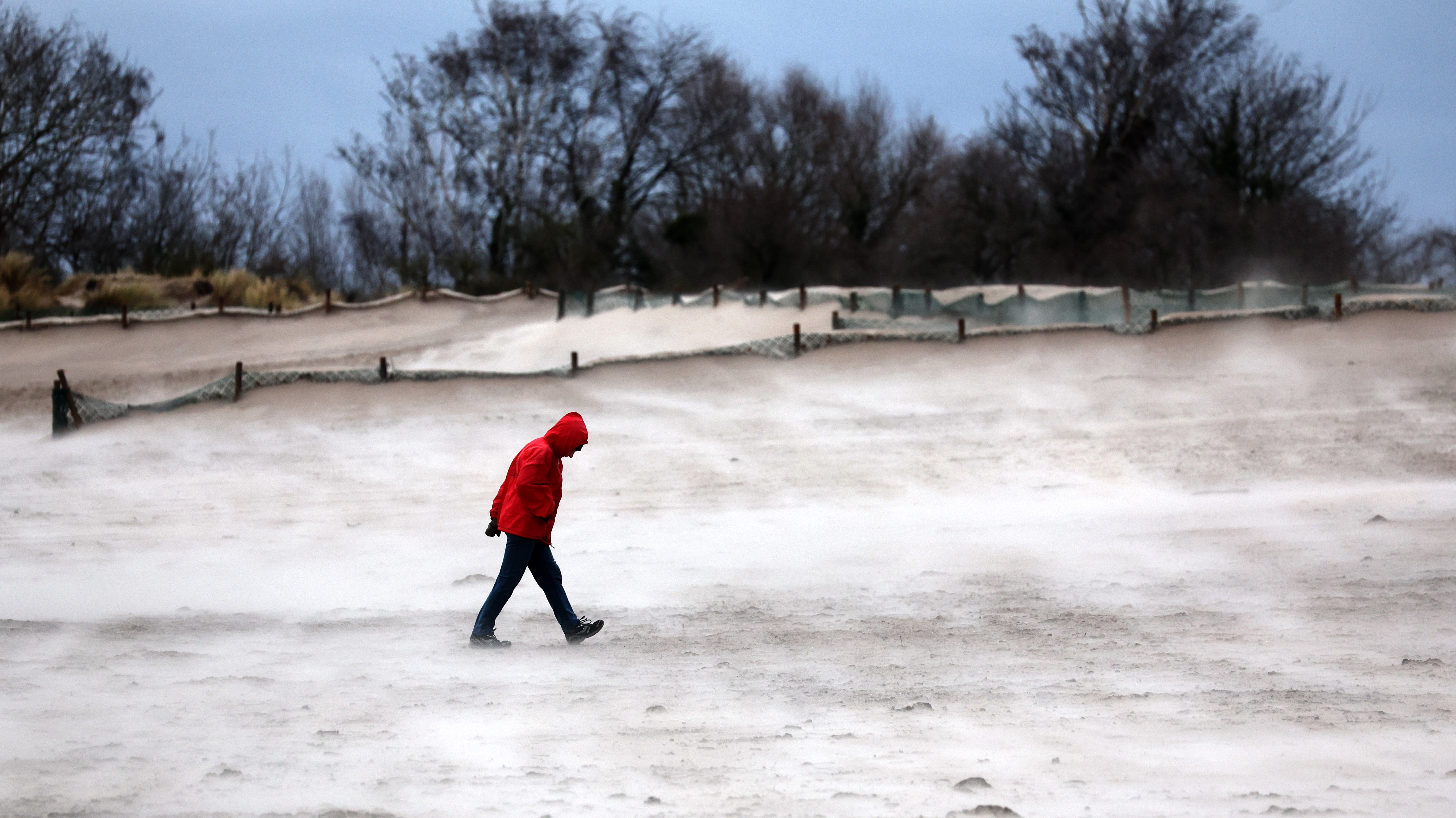 21.12.2023, Mecklenburg-Vorpommern, Warnem&uuml;nde: Ein Mann geht im Sturm am Ostseestrand entlang, der vom Wind verwehte Sand leuchtet hell. (Bernd W&uuml;stneck/dpa)