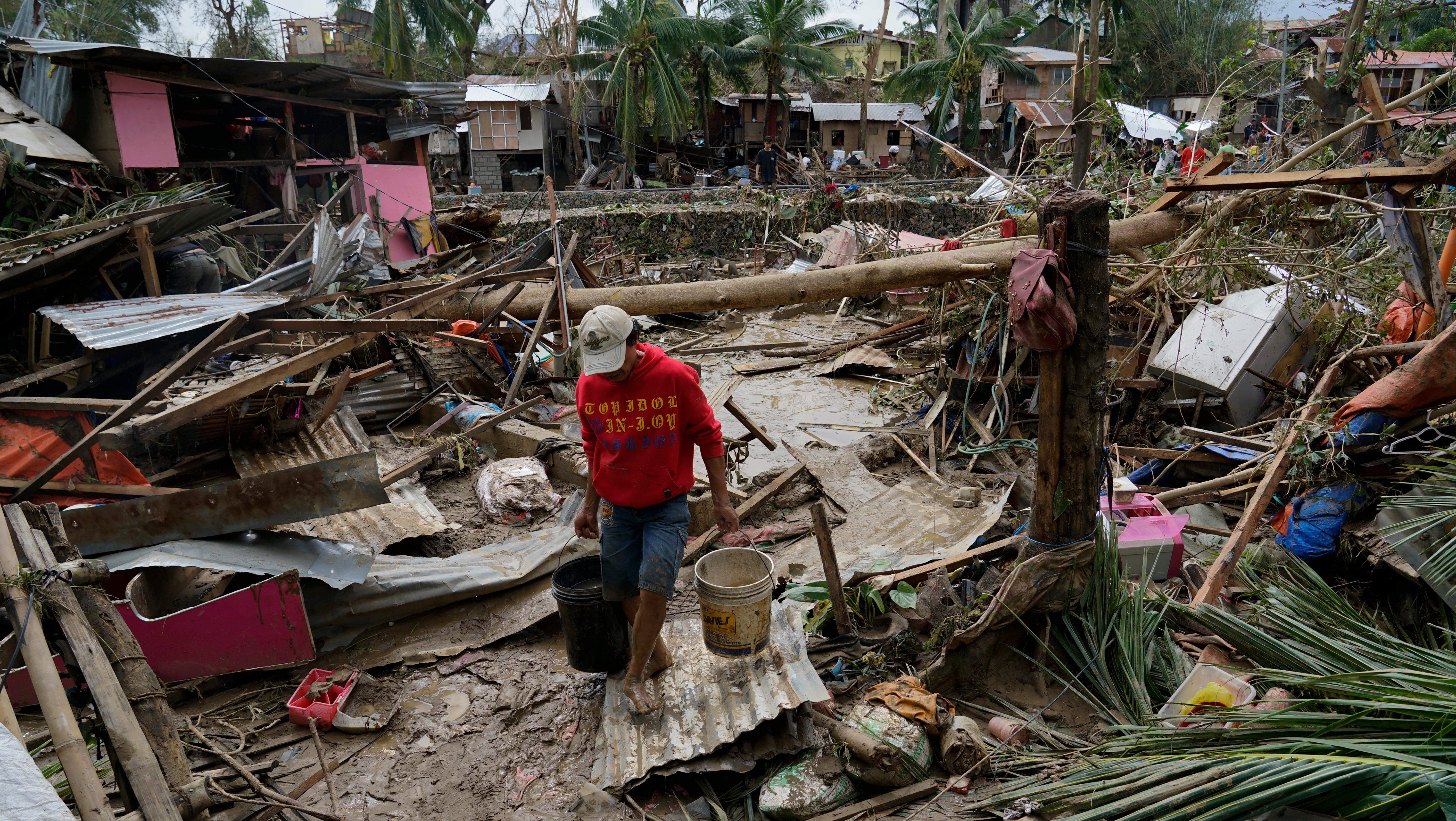 Philippinen, Talisay: Ein Mann tr&auml;gt Eimer in einer durch Taifun Rai verw&uuml;steten Region. Der Taifun Rai hat auf den Philippinen schwere Verw&uuml;stungen angerichtet und mehr als 300 000 Menschen in die Flucht getrieben. Der Tropensturm habe nicht nur &Uuml;berschwemmungen, Sturzfluten und Erdrutsche ausgel&ouml;st, sondern auch D&auml;cher abgedeckt und zahlreiche B&auml;ume und Strommasten aus dem Boden gerissen, teilte der Katastrophenschutz am Freitag mit.