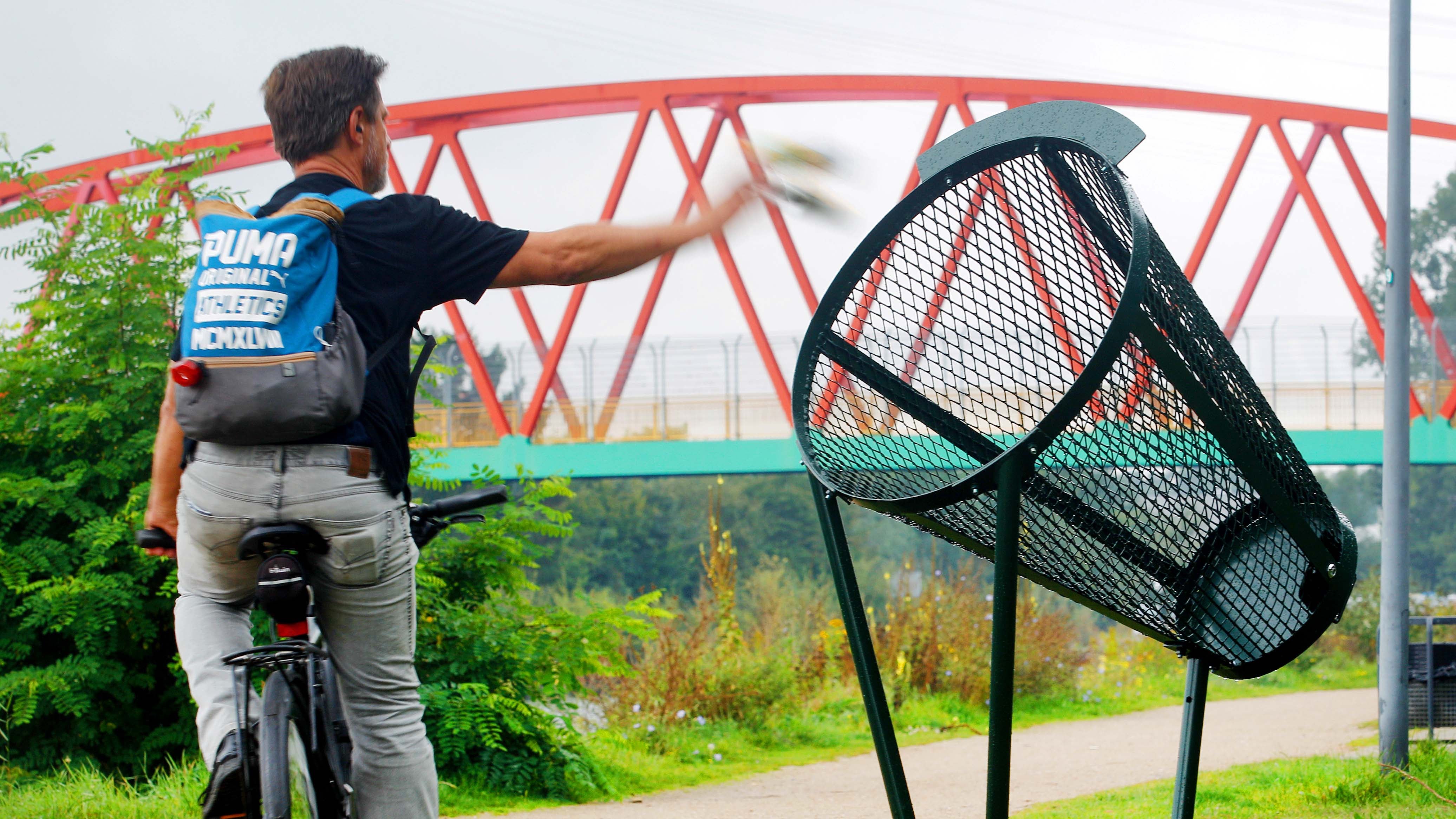 15.09.2021, Nordrhein-Westfalen, Herne: Ein Fahrradfahrer wirft am Rhein-Herne-Kanal seinen M&cedil;ll im Vorbeifahren in einen der neuen Wurfm&cedil;lleimer. Die Idee dahinter ist, dass die Radfahrer nicht absteigen m&cedil;ssen, um ihren M&cedil;ll zu entsorgen. Foto: Roland Weihrauch/dpa +++ dpa-Bildfunk +++