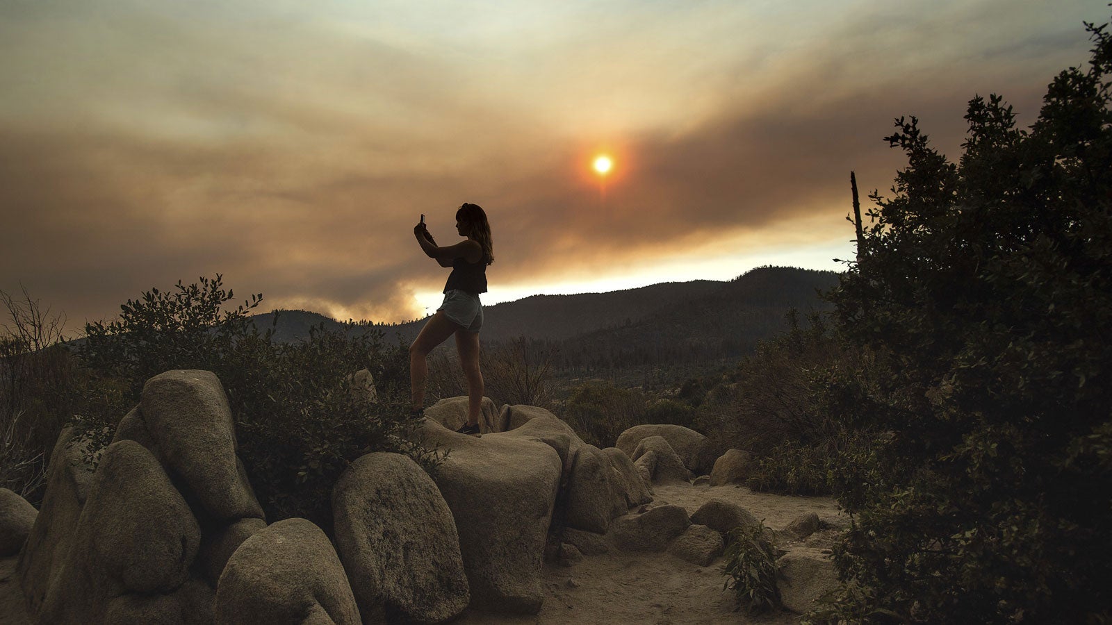 ARCHIV - 25.07.2018, USA, Yosemite National Park: Mara Schumann fotografiert eine Rauchwolke eines Waldbrandes &uuml;ber dem Yosemite Nationalpark in Kalifornien. (zu dpa &laquo;Kalifornien verbietet Rauchen an Str&auml;nden und in Naturparks&raquo;) Foto: Noah Berger/AP/dpa +++ dpa-Bildfunk +++