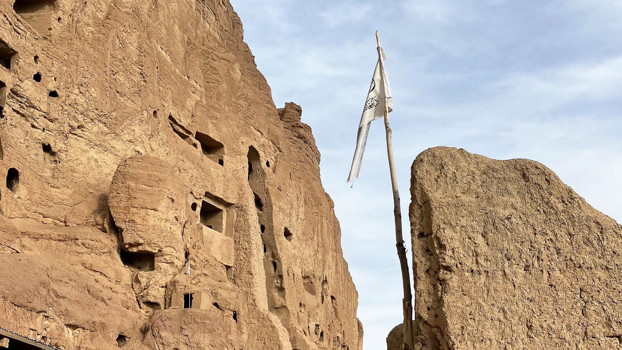 15.11.2025, Afghanistan, Bamian: Eine Taliban-Flagge weht nahe der &Uuml;berreste der von den Taliban gesprengten Buddha-Statuen von Bamian. (Nabila Lalee/dpa)

