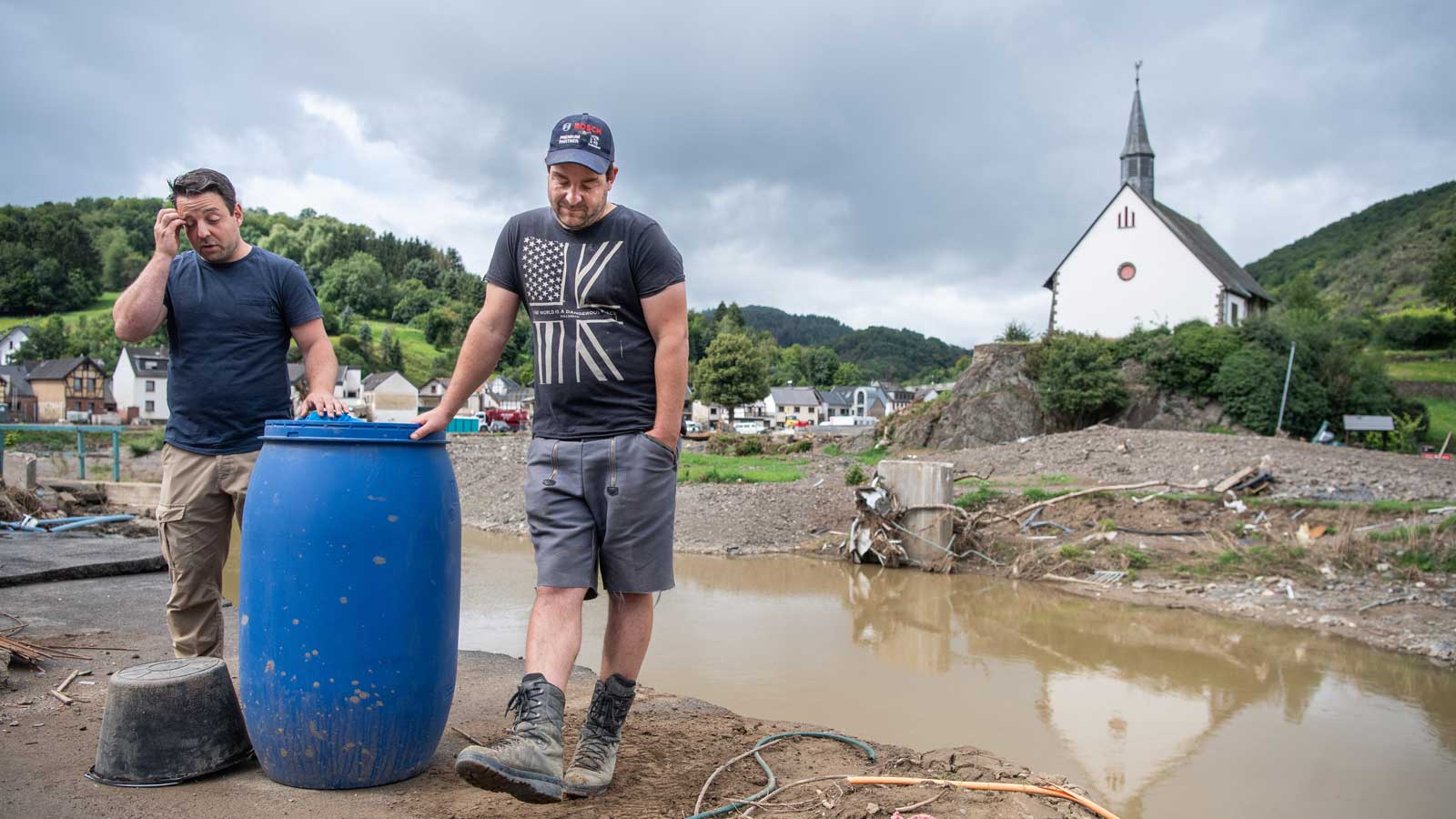 ARCHIV - 21.08.2021, Rheinland-Pfalz, Altenahr: Achim (l) und Oliver Gasper stehen am Ufer der Ahr und ruhen sich einen Moment von den Aufr&auml;umarbeiten an ihren H&auml;usern aus (zu dpa &laquo;Lotsen helfen im Ahrtal - &laquo;Die schweren F&auml;lle melden sich nicht&raquo;). Foto: Boris Roessler/dpa +++ dpa-Bildfunk +++
