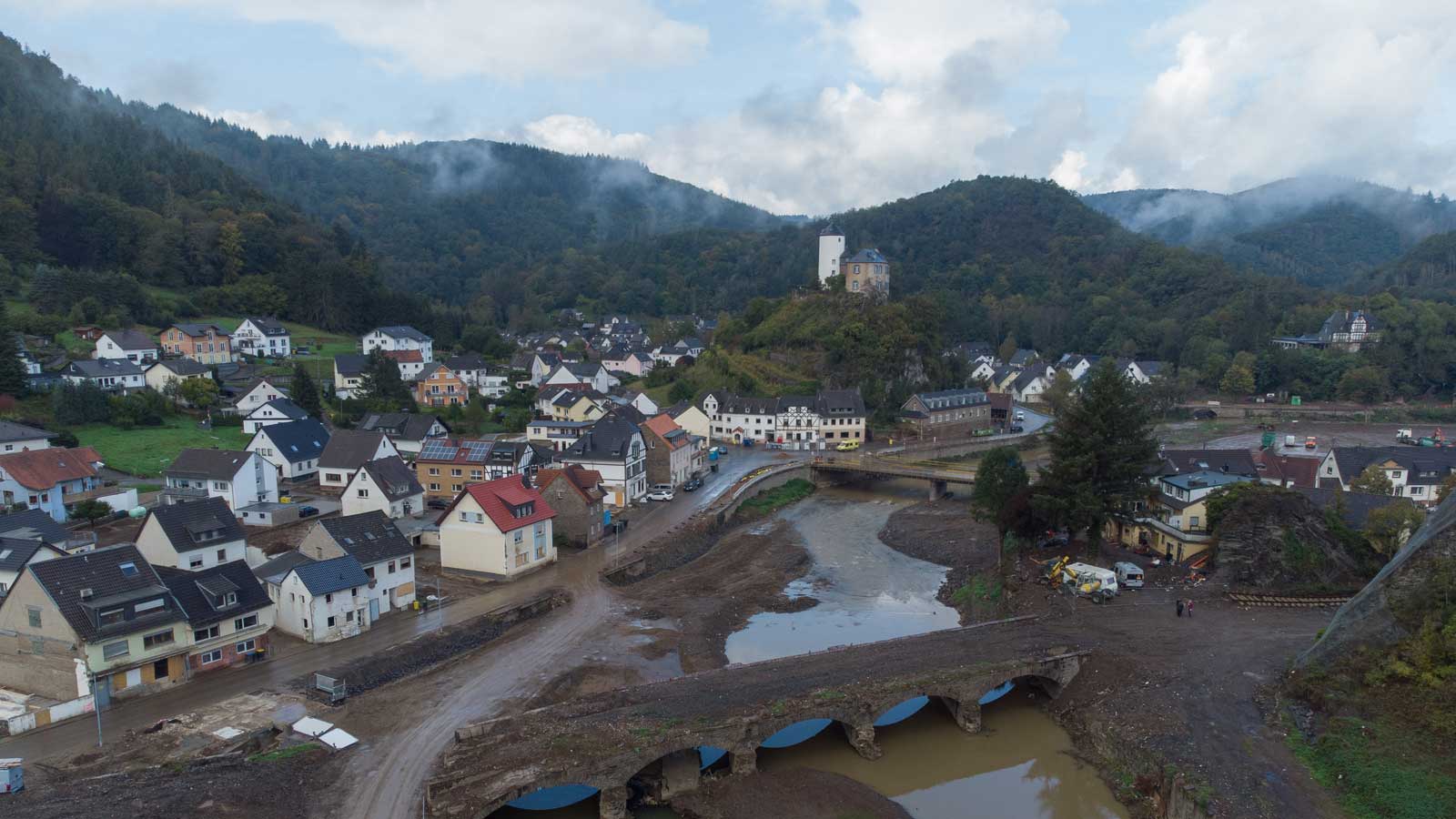 ARCHIV - 08.10.2021, Rheinland-Pfalz, Altenahr-Kreuzberg: Mittlerweile von Tr&uuml;mmern befreit ist die bei der Flut zerst&ouml;rten, historische Bogenbr&uuml;cke &uuml;ber die Ahr in Altenahr-Kreuzberg (Luftaufnahme mit einer Drohne). Zahlreiche H&auml;user am Ufer der Ahr waren bei der Katastrophe so stark besch&auml;digt worden, dass sie mittlerweile abgerissen werden mussten. (Zu dpa &laquo;Lotsen helfen im Ahrtal - &laquo;Die schweren F&auml;lle melden sich nicht&raquo;&raquo;). Foto: Boris Roessler/dpa +++ dpa-Bildfunk +++