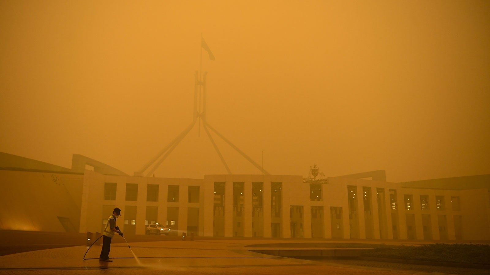 05.01.2020, Australien, Canberra: Ein Mann s&auml;ubert am fr&uuml;hen Morgen den Vorplatz des Parlamentsgeb&auml;udes inmitten von Rauchschwaden, die von den verheerenden Buschbr&auml;nden verursacht wurden. Foto: Lukas Coch/AAP/dpa 