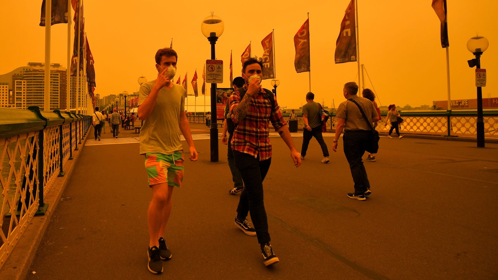 06.12.2019, Australien, Sydney: Fu&szlig;g&auml;nger tragen Atemschutzmasken, w&auml;hrend sie unter den Rauchschwaden der nahen Buschbr&auml;nde &uuml;ber eine Br&uuml;cke gehen. Foto: Paul Braven/AAP/dpa +++ dpa-Bildfunk +++