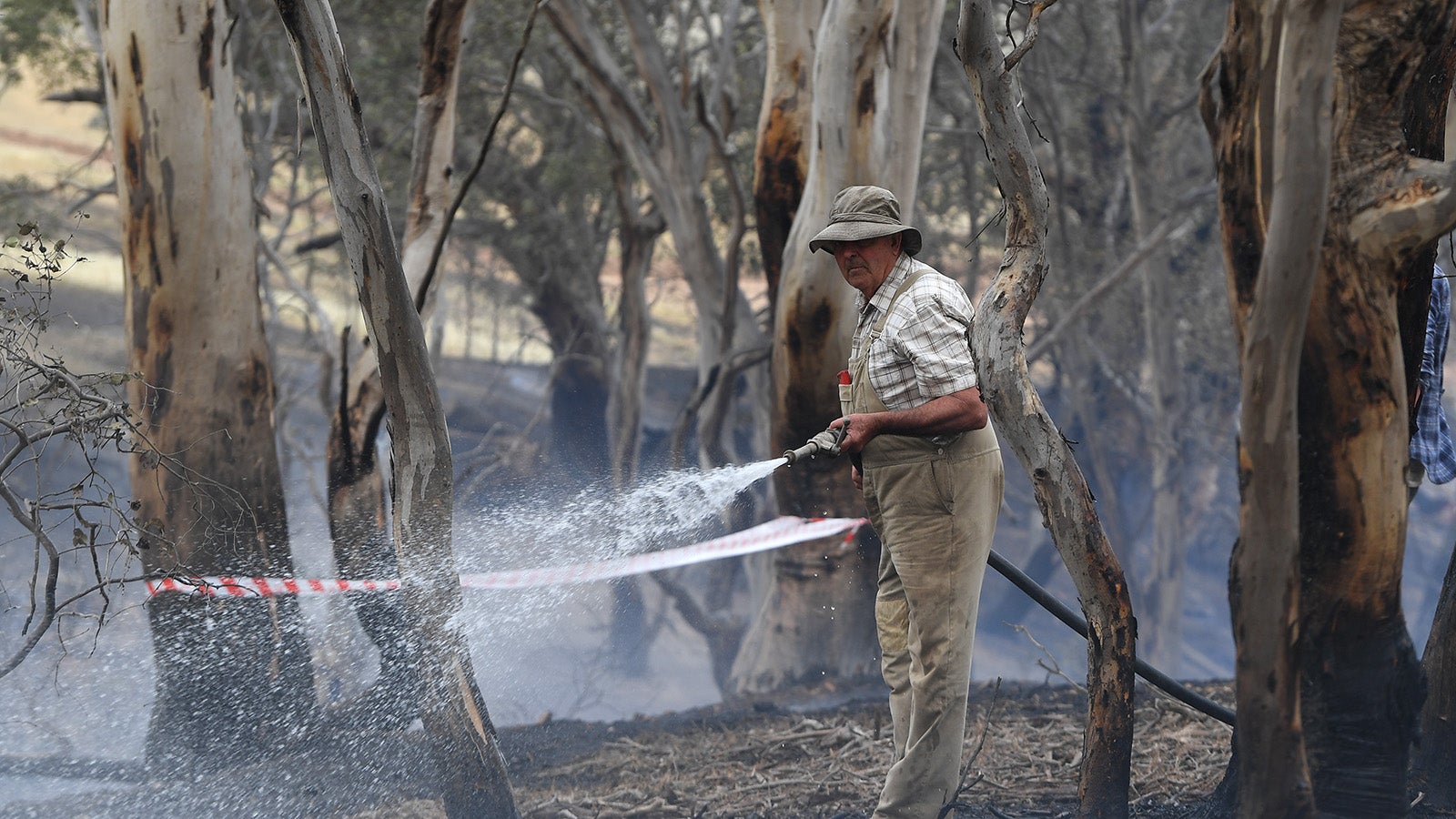 21.11.2019, Australien, Melbourne: Tom Davies spritzt Wasser auf schwelendes Buschland am Mount Glasgow. Foto: James Ross/AAP/dpa +++ dpa-Bildfunk +++