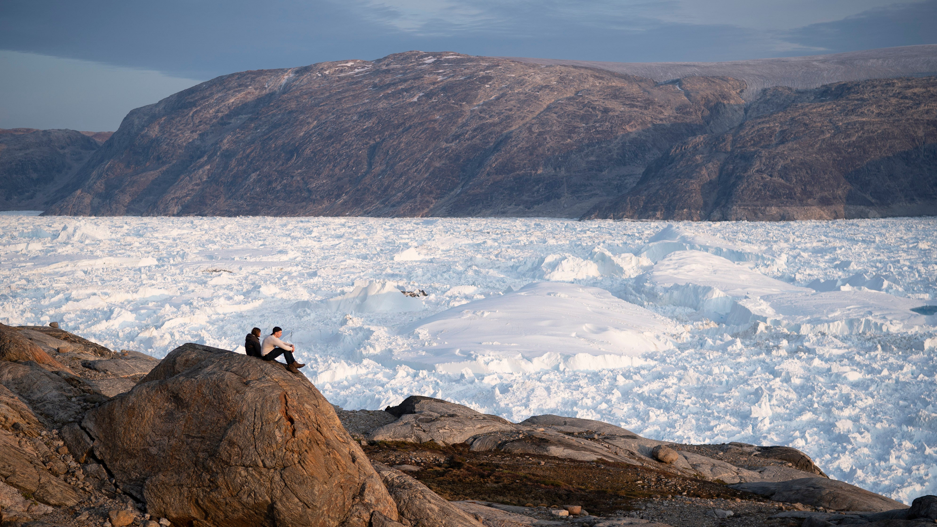Gr&ouml;nland, Helheim Glacier: Zwei Studenten der New York University, die hier an einer Forschungsexkursion teilnehmen, sitzen auf einem Felsen mit Blick auf den Helheim-Gletscher. Am h&ouml;chsten Punkt des gr&ouml;nl&auml;ndischen Eisschildes hat es am Wochenende zum ersten Mal seit Beginn der Wetteraufzeichnungen geregnet.