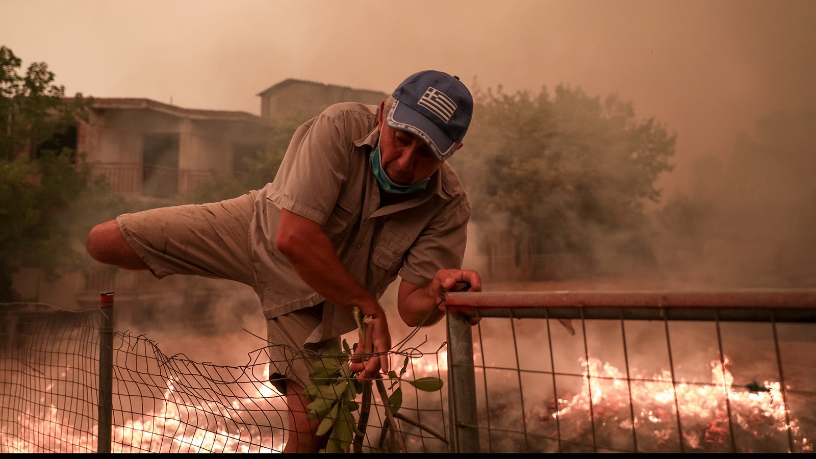 08.08.2021, Griechenland, Evia Island: Ein Mann rettet sich w&auml;hrend der L&ouml;scharbeiten eines Waldbrandes im Dorf Pefki auf der Insel Eub&ouml;a &uuml;ber einen Zaun. Die Lage wird immer bedrohlicher: Auf der griechischen Insel Eub&ouml;a stehen auch am siebten Tag gewaltige Waldfl&auml;chen in Flammen, die Br&auml;nde breiten sich unkontrolliert aus. Foto: Eurokinissi/Eurokinissi via ZUMA Press Wire/dpa +++ dpa-Bildfunk +++