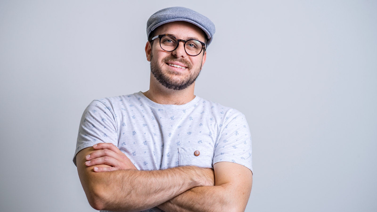 Portrait of confident creative businessman and entrepreneur against gray background. Male entrepreneur is smiling while standing with arms crossed. He is in smart casuals.