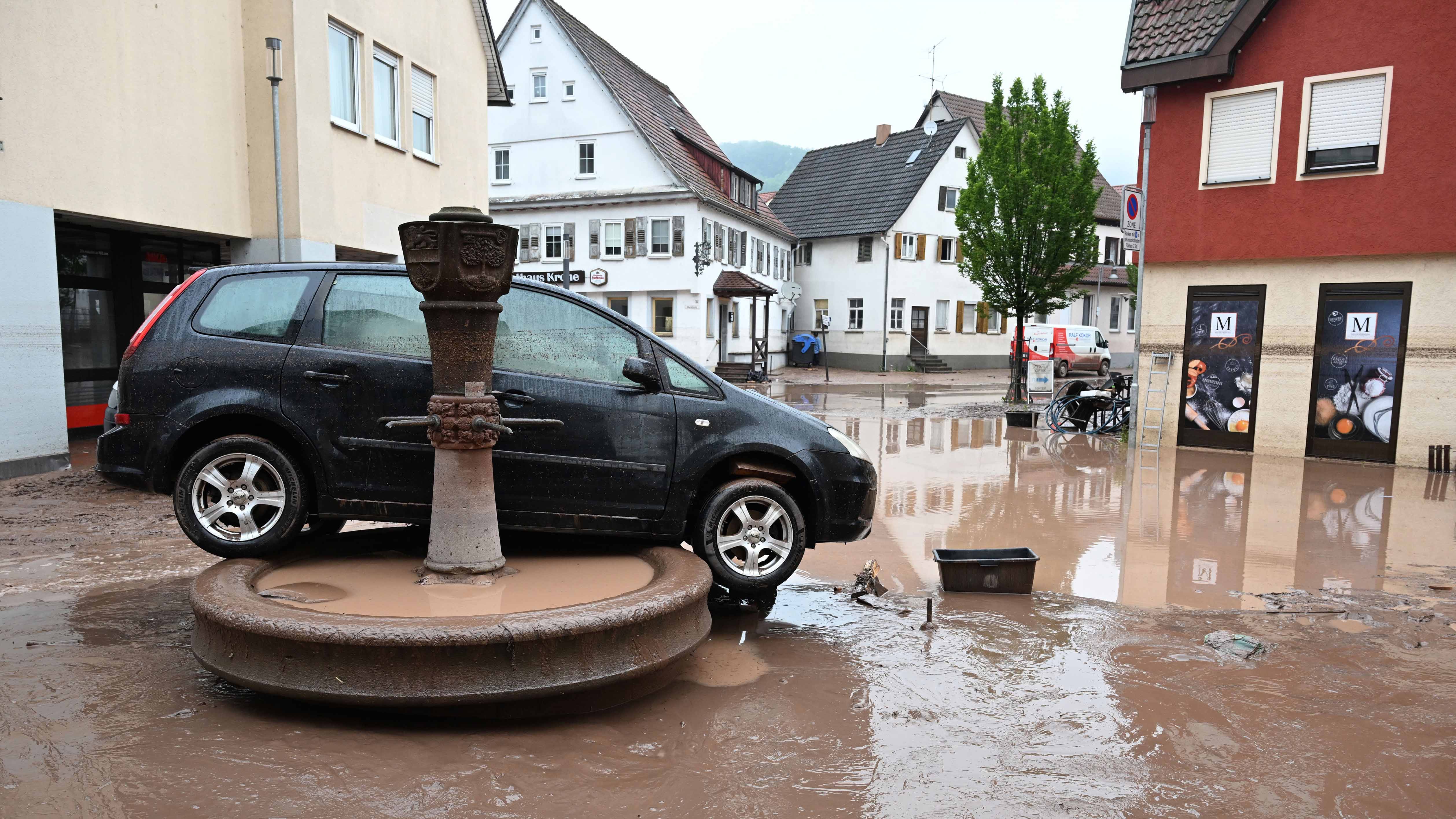 ARCHIV - 06.09.2024, Baden-W&cedil;rttemberg, Rudersberg: KOMBO - Blick auf den Brunnen in Rudersberg (oben, Archivfoto vom 03.06.2024) und unten, rund 100 Tage nach der Hochwasser-Katastrophe im Rems-Murr-Kreis. Vor rund 100 Tagen wurde der Platz und der Brunnen nach einem Hochwasser &cedil;berflutet und ein Auto war auf den Brunnen gesp&cedil;lt worden. Der Wiederaufbau nach dem Hochwasser hat gerade erst angefangen - und wird wohl noch Jahre dauern. (zu dpa: &acute;100 Tage nach dem Hochwasser - Wiederaufbau erst am Anfang&ordf;) Foto: Bernd Weiﬂbrod/dpa +++ dpa-Bildfunk +++