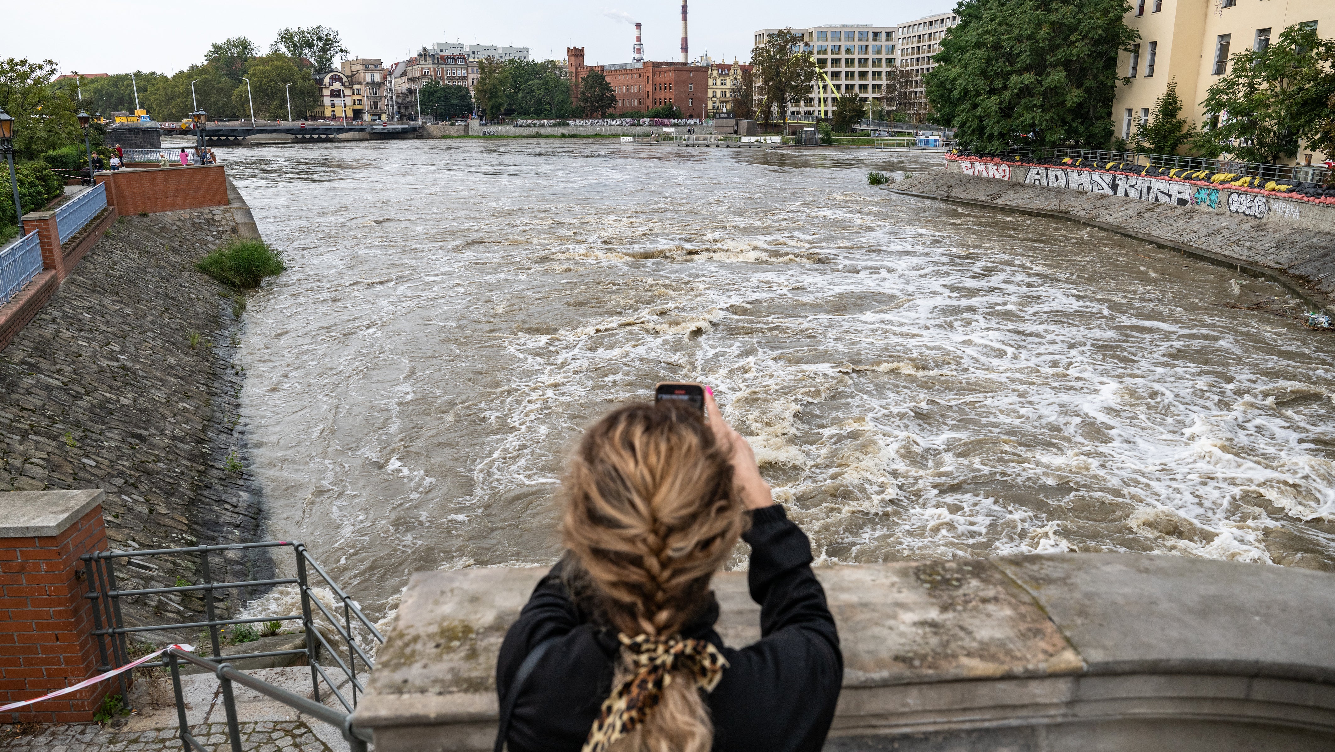 19.09.2024, Polen, Breslau: Eine Frau fotografiert die Wasserscheide der Oder im Stadtzentrum. Seit dem 13. September sind Regionen in Mittel- und Osteuropa von den verheerenden &Uuml;berschwemmungen durch den Sturm Boris schwer betroffen (Tane&egrave;ek David/CTK/dpa)


