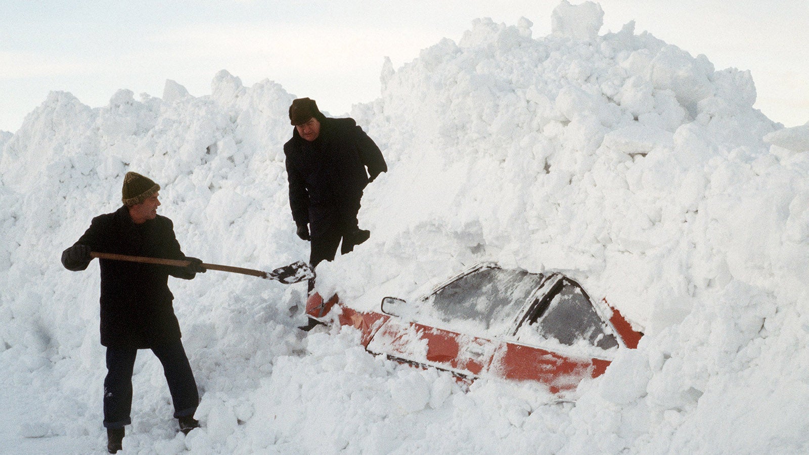1. Januar 1979:  Zwei M&auml;nner graben mit einer Schaufel ein Auto aus den Schneemassen. Schleswig-Holstein erlebt eine der gr&ouml;&szlig;ten Schneekatastrophen in der Geschichte des Landes. St&auml;dte und D&ouml;rfer waren von der Au&szlig;enwelt abgeschnitten, der Zugverkehr kam zum Erliegen und auf Autobahnen t&uuml;rmten sich meterhohe Schneemassen auf.  Foto: Georg Spring/dpa 