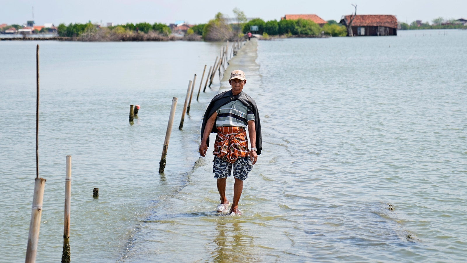 A man walks on a pathway that is partially submerged due to the rising sea levels in the village of Sidogemah, Central Java, Indonesia, Sunday, Nov. 7, 2021. World leaders are gathered in Scotland at a United Nations climate summit, known as COP26, to push nations to ratchet up their efforts to curb climate change. Experts say the amount of energy unleashed by planetary warming would melt much of the planet's ice, raise global sea levels and greatly increase the likelihood and extreme weather events. (AP Photo/Dita Alangkara)