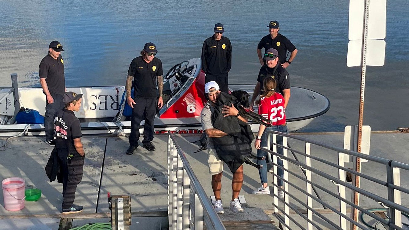 Dieses Foto, das von der Feuerwehr von San Diego ver&ouml;ffentlicht wurde, zeigt Sadie, eine schwarze Labrador-Mischlingsh&uuml;ndin, wie sie von ihren Eltern Brandon und Alexis am 23. November 2025 abgeholt wird. (San Diego Fire-Rescue via AP)