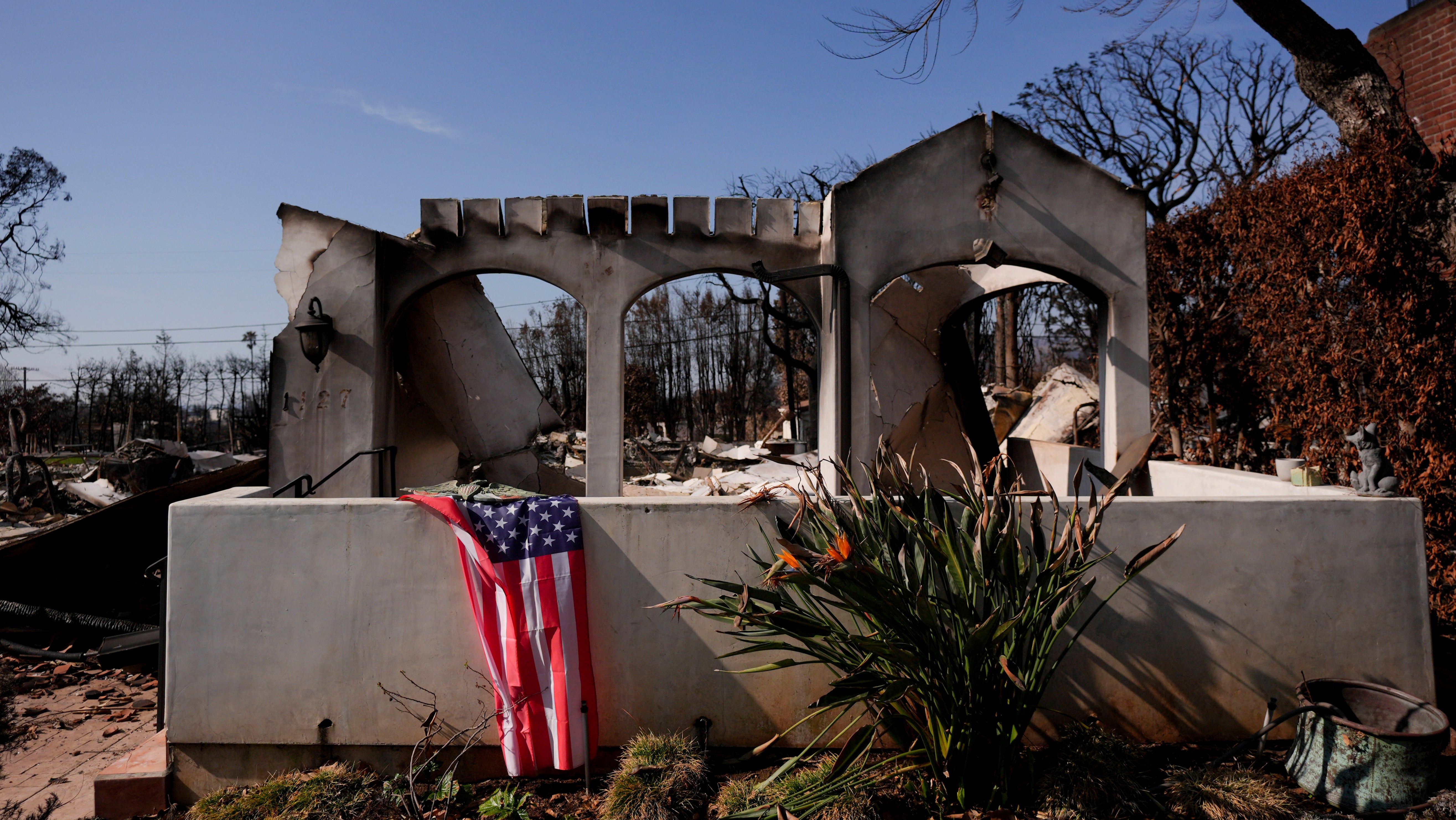 28.01.2025, USA, Los Angeles: Eine US-Flagge ist vor einem vom Feuer verw&uuml;steten Grundst&uuml;ck in der Brandzone des Palisades-Feuers im Stadtteil Pacific Palisades von Los Angeles drapiert. (Jae C. Hong/AP/dpa)