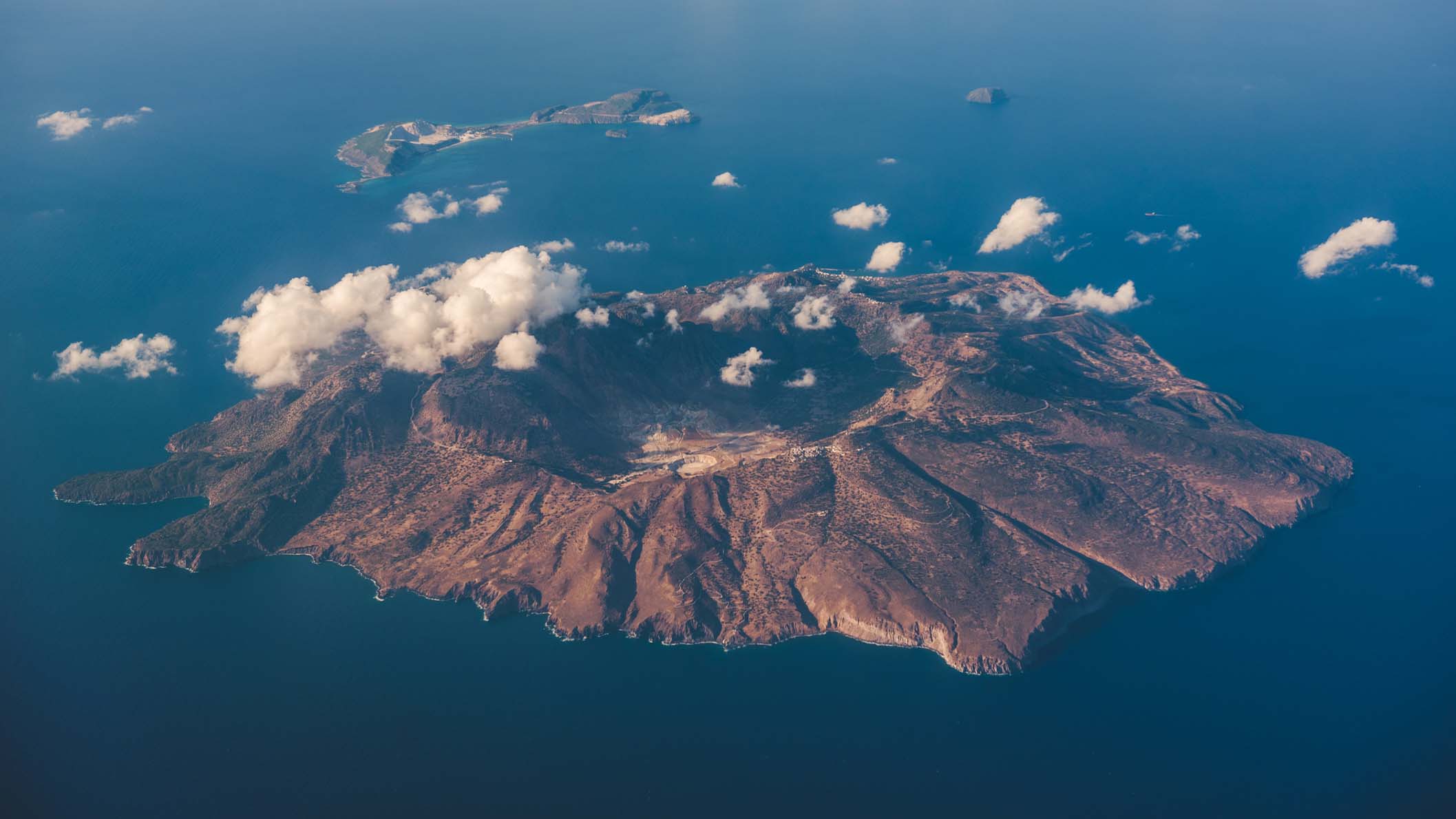 Aerial view over Nisyros island, Greece. Nisyros is a volcanic Greek island and municipality located in the Aegean Sea. It is part of the Dodecanese group of islands, situated between the islands of Kos and Tilos.Its shape is approximately round, with a diameter of about 8 km and an area of 41.6 km2. Several other islets are found in the direct vicinity of Nisyros, the largest of which is Gyali, with a population of 22 citizens.