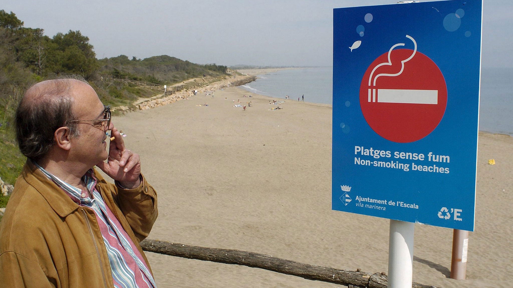  14.04.2006, Spanien, Katalonien, L'Escala: Ein Mann raucht, w&auml;hrend er die Aufschrift auf einem Schild am Strand von l'Escala bei Girona im Nordosten Spaniens liest. Auf dem Schild steht geschrieben: &laquo;Nichtraucher-Str&auml;nde&raquo;. Kippen an Str&auml;nden sind in Spanien weiterhin unerw&uuml;nscht. Derzeit werden Rufe nach &laquo;playas sin humo&raquo; (rauchfreien Str&auml;nden) immer lauter, um speziell Familien mit Kindern w&auml;hrend der Ferien ein Ambiente ohne Rauch und Zigarettenstummeln zu garantieren. (zu dpa Kampf den Kippen: Mittelmeerstr&auml;nde mutieren zu Nichtraucherzonen vom 09.09.2018) Foto: Robin Townsend/EFE/dpa +++ dpa-Bildfunk +++ 
