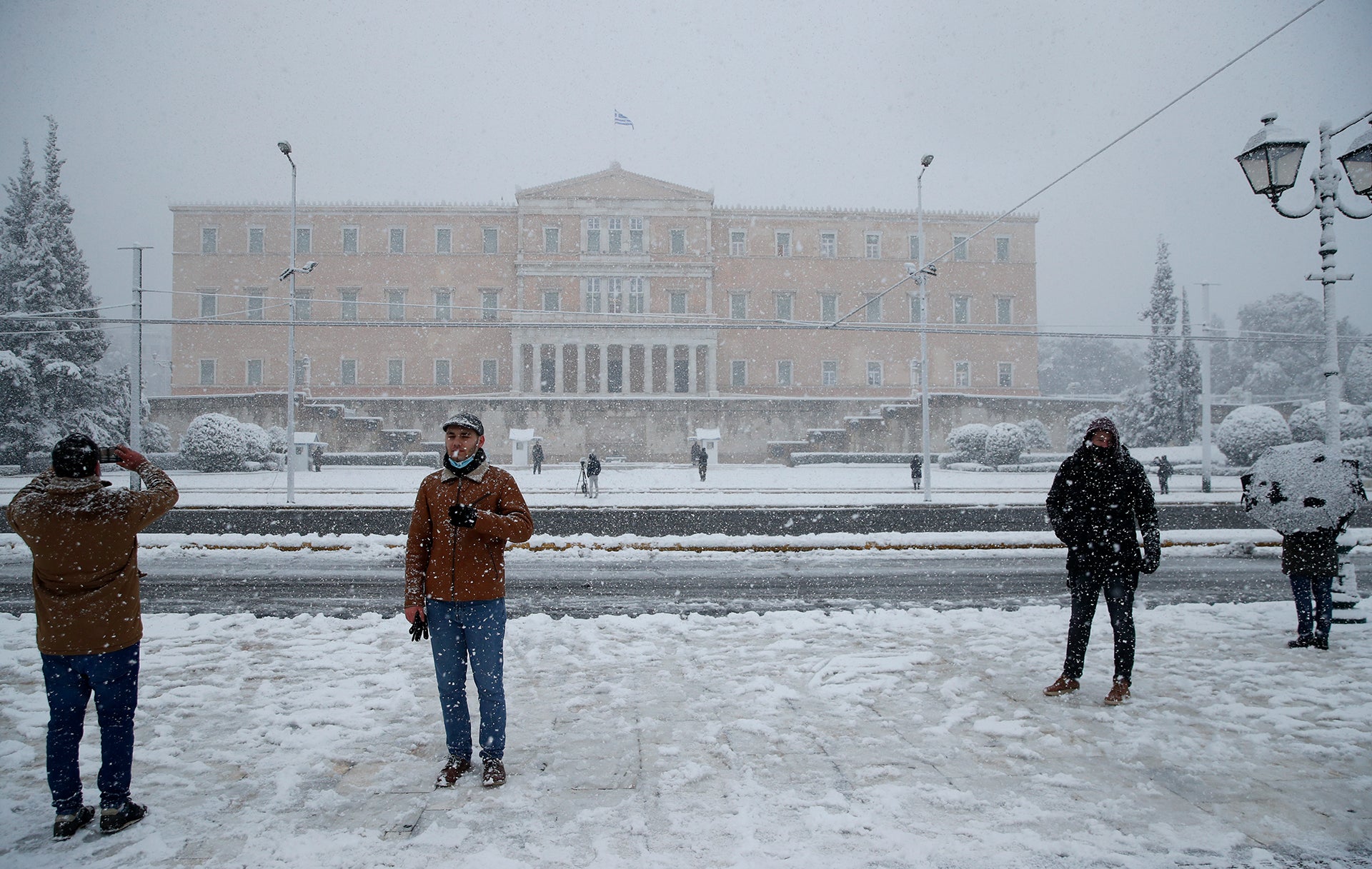 16.02.2021, Griechenland, Athen: Menschen fotografieren, w&auml;hrend &uuml;ber dem griechischen Parlament in Athen Schnee f&auml;llt. Die K&auml;ltefront &laquo;Medea&raquo; hat mit starken Schneef&auml;llen chaotische Zust&auml;nde in weiten Teilen Griechenlands verursacht. Sogar auf der Akropolis in Athen lag nach stundenlangen Schneeschauern am Dienstagmorgen eine etwa zehn Zentimeter dicke Schneedecke, wie das Staatsfernsehen ERT berichtete. Foto: Thanassis Stavrakis/AP/dpa +++ dpa-Bildfunk +++
