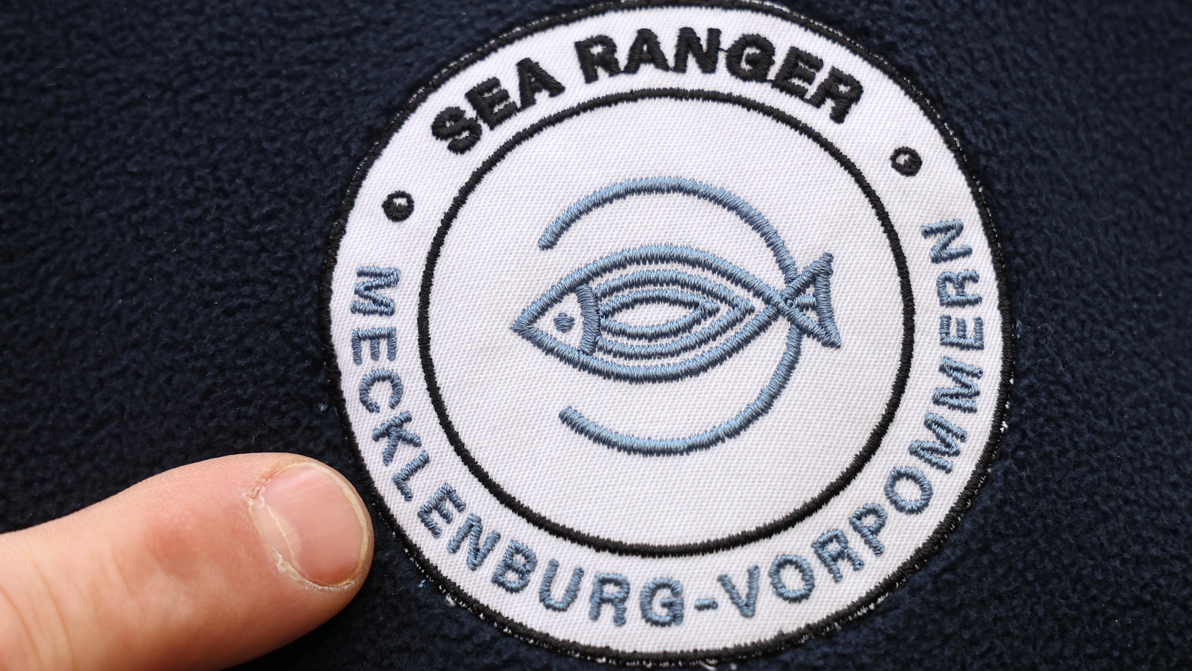 14.02.2024, Mecklenburg-Vorpommern, K&uuml;hlungsborn: An Bord des Fischereiforschungsschiffes Solea auf der Ostsee zeigt Fischer H&ouml;pfner aus Garz auf Usedom auf das Logo "Sea Ranger" auf seiner Jacke. (Bernd W&uuml;stneck/dpa)

