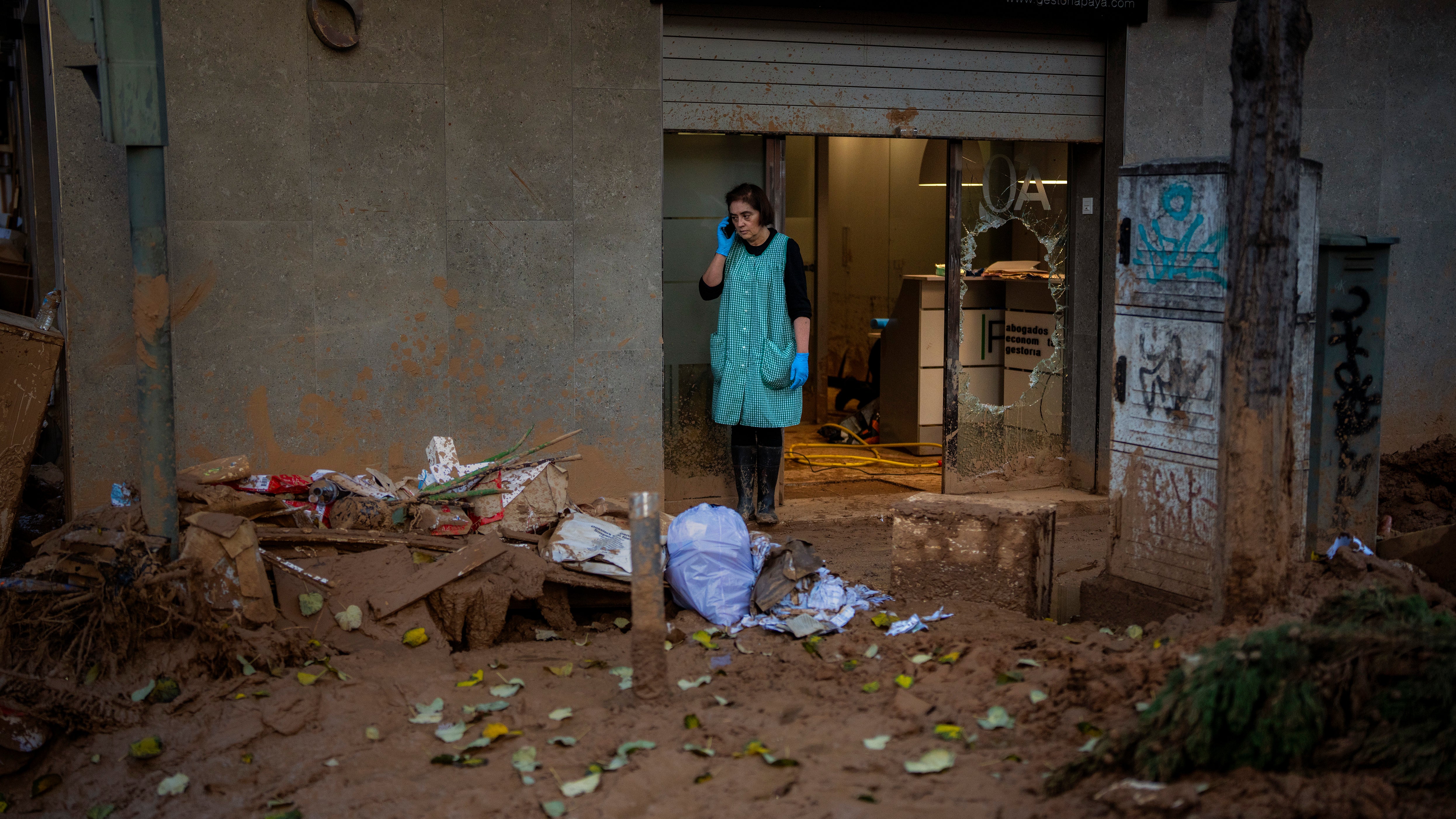 07.11.2024, Spanien, Masanasa: Eine Frau telefoniert am Eingang eines von &Uuml;berschwemmungen betroffenen Gesch&auml;fts. (Emilio Morenatti/AP/dpa)