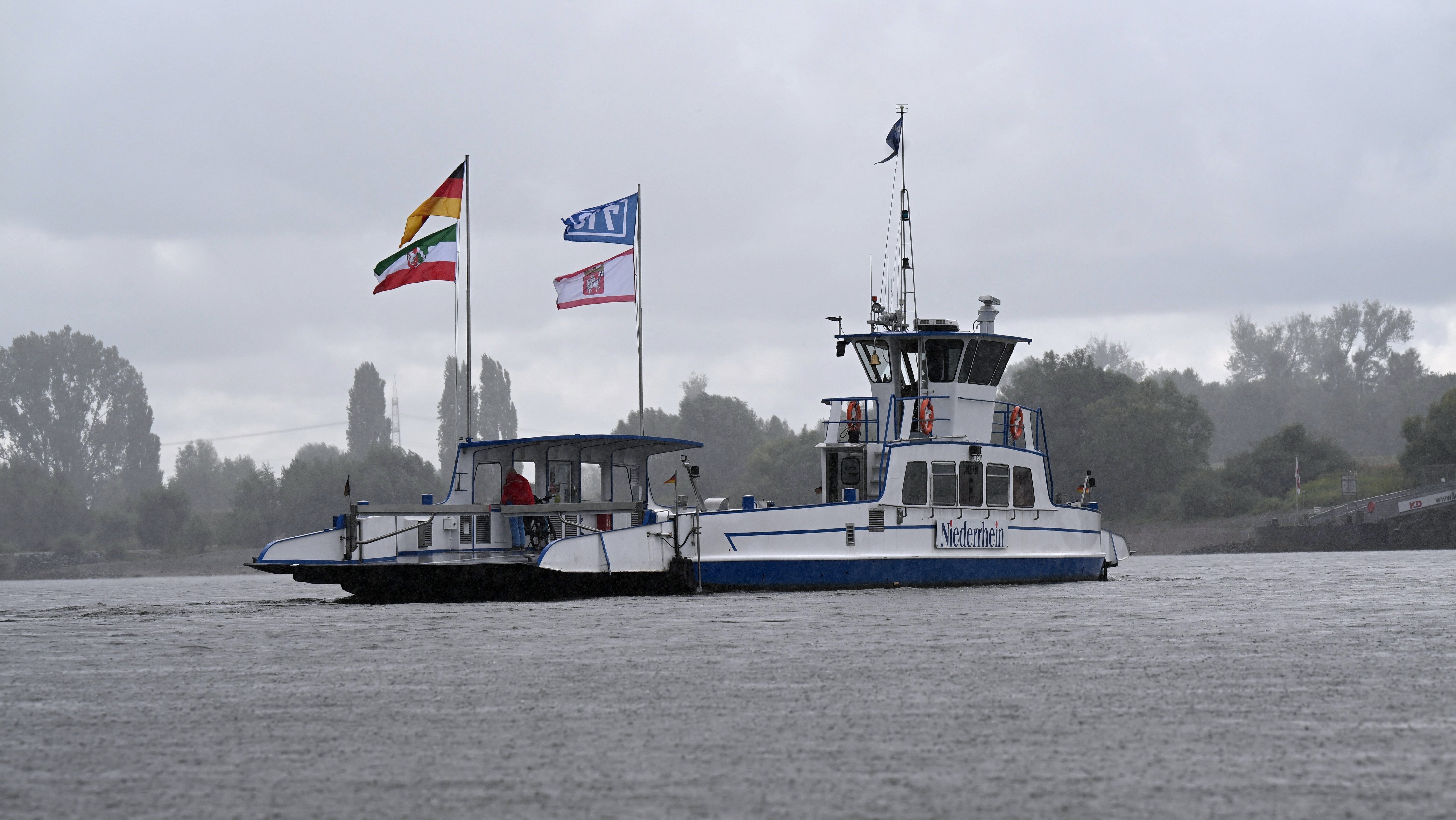 22.08.2026, NA, D&uuml;sseldorf: Eine fast leere F&auml;hre f&uuml;r Autos und Personen f&auml;hrt bei Regenwetter zwischen dem D&uuml;sseldorfer S&uuml;den (Urdenbach) und dem beliebten Ausflugsziel Zons (Dormagen) auf dem Rhein. Nach 29 Tagen Zwangspausen wegen des Niedrigwassers konnten die Rheinf&auml;hrbetriebe Jansen den Betrieb wieder aufnehmen, andere Rheinf&auml;hren konnten ebenfalls wieder starten. (Wolf von Dewitz/dpa)