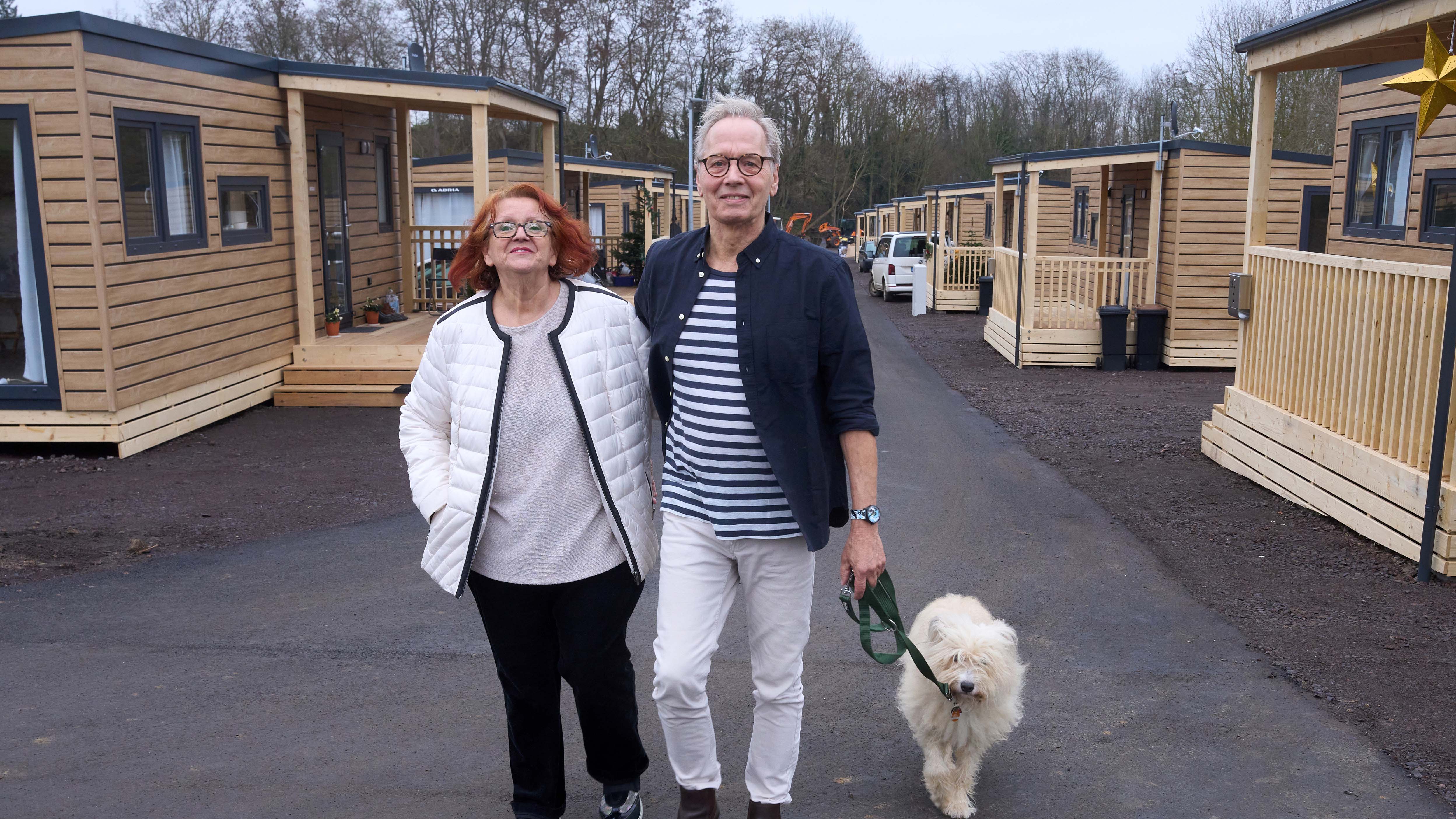 14.12.2021, Rheinland-Pfalz, Grafschaft: Doris und Peter Bruch spazieren an Tiny-Houses vorbei. Eines davon haben sie vor wenigen Tagen bezogen. Die Sturzflut in der Nacht auf den 15. Juli ist auch durch das komplette Erdgeschoss in ihrem Reihenhaus in Bad Neuenahr-Ahrweiler gestr&ouml;mt. Bis ihr Haus wieder bewohnbar ist, sind die beiden in einem Tiny-Haus untergekommen. (zu dpa &laquo;&laquo;Endlich was Eigenst&auml;ndiges&raquo; - Minih&auml;user f&uuml;r Flutopfer&raquo;) Foto: Thomas Frey/dpa +++ dpa-Bildfunk +++