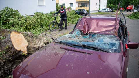 21.05.2022, Nordrhein-Westfalen, Lippstadt: Ein Mann geht an einem durch einen umgest¸rzten Baum zerstˆrten Auto vorbei. Einen Tag nach dem Tornado haben in der Stadt die Aufr‰umarbeiten begonnen. Foto: Lino Mirgeler/dpa +++ dpa-Bildfunk +++