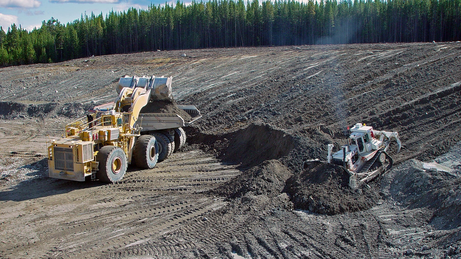 "Mining equipment (loader, truck, and dozer) working to remove overburden for reclamation."