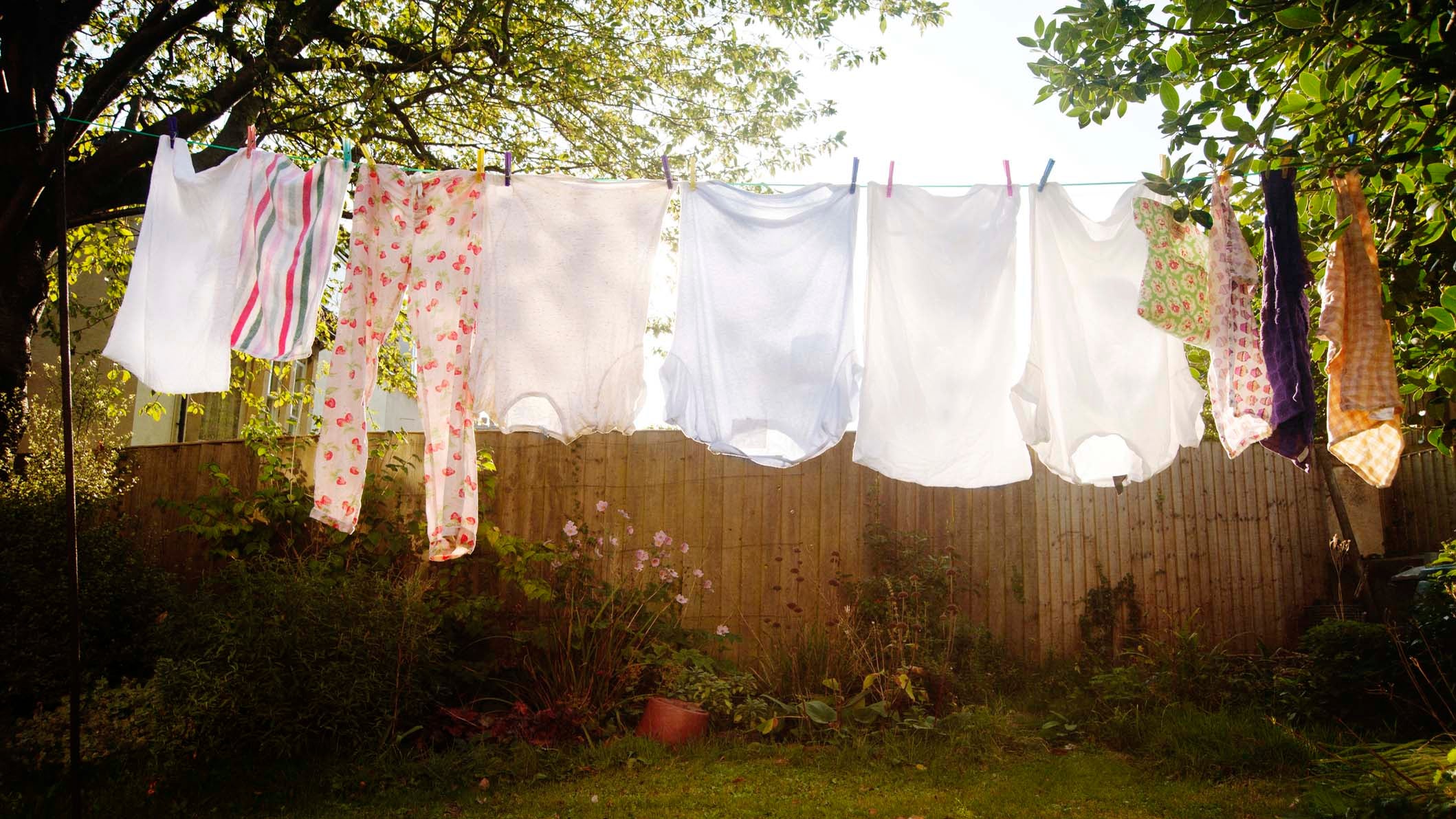 Freshly laundered clothes hang out to dry on a washing line, backlit by the early morning sunlight in an urban garden the city of Bristol, England.