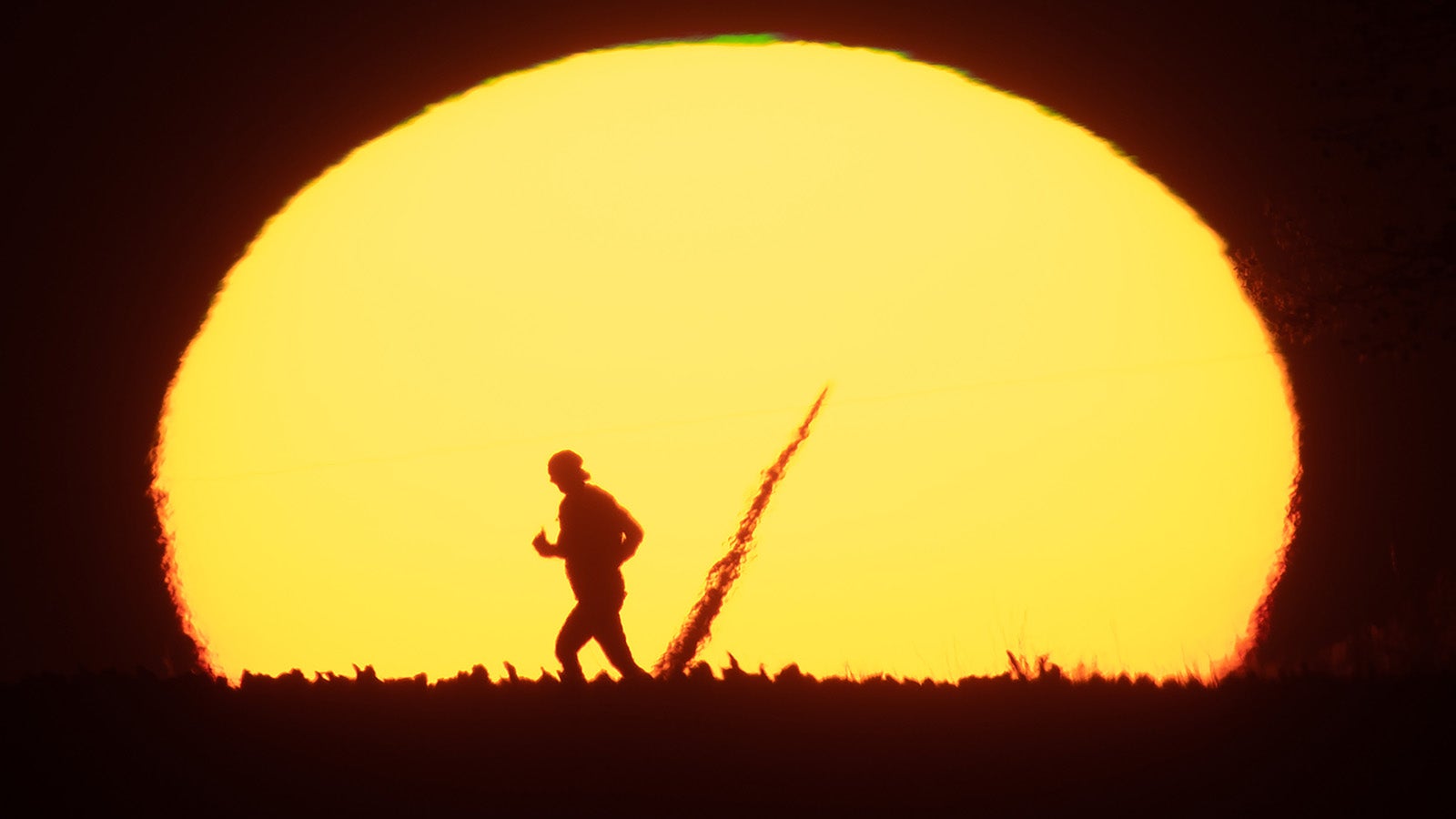 ARCHIV - 21.09.2020, Niedersachsen, Algermissen: Eine Frau joggt am fr&uuml;hen Morgen beim Sonnenaufgang &uuml;ber einen Feldweg im Landkreis Hildesheim. In der Sonne ist zudem ein Rotorblatt eines Windrades zu erkennen. (zu dpa &laquo;NOAA: Vergangener Monat war w&auml;rmster September seit Messungsbeginn&raquo;) Foto: Julian Stratenschulte/dpa +++ dpa-Bildfunk +++