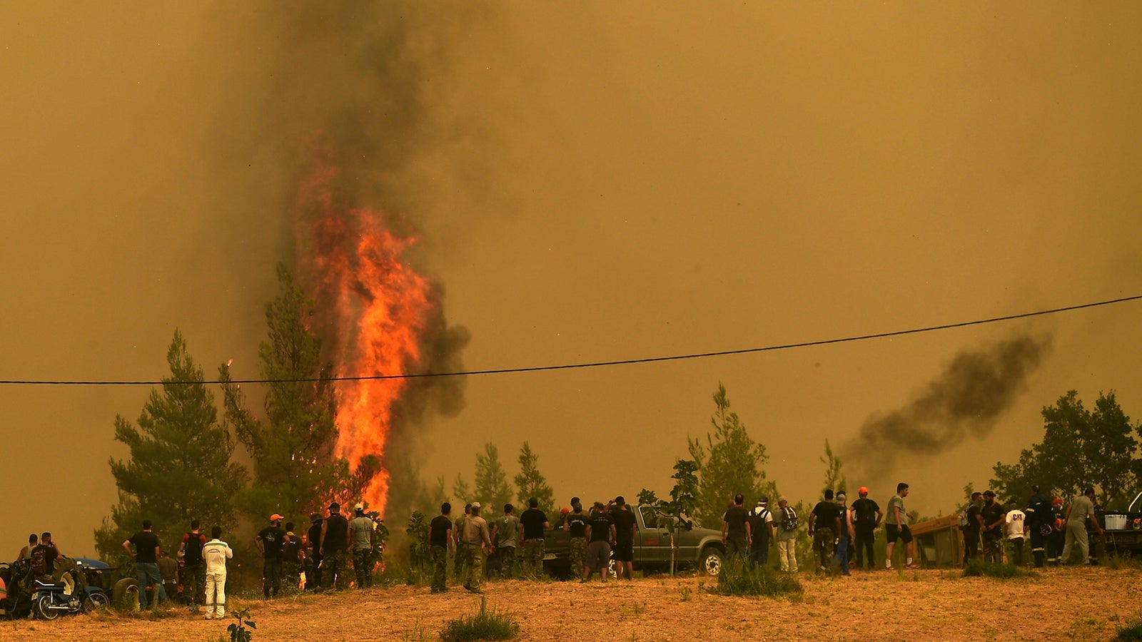 09.08.2021, Griechenland, Evia: Menschen beobachten die Flammen, die B&auml;ume w&auml;hrend eines Waldbrandes im Dorf Avgaria auf der Insel Eub&ouml;a verbrennen. Feuerwehrleute und Anwohner k&auml;mpften am Montag einen siebten Tag lang gegen einen massiven Waldbrand auf der zweitgr&ouml;&szlig;ten griechischen Insel und versuchten, so viel wie m&ouml;glich aus den Flammen zu retten, die weite Teile des unber&uuml;hrten Waldes vernichtet, H&auml;user und Gesch&auml;fte zerst&ouml;rt und Tausende in die Flucht getrieben haben. Foto: Michael Varaklas/AP/dpa +++ dpa-Bildfunk +++