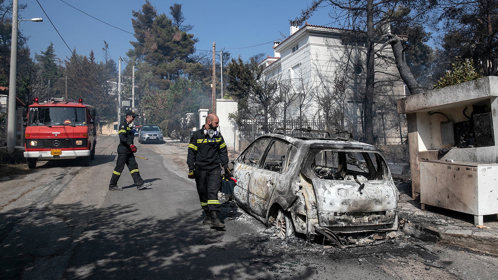 Firefighters look at a burnt car following a forest fire at Dionysos northern suburb of Athens, on Tuesday, July 27, 2021. Greek authorities have evacuated several areas north of Athens as a wildfire swept through a hillside forest and threatened homes despite a large operation mounted by firefighters. (AP Photo/Yorgos Karahalis)