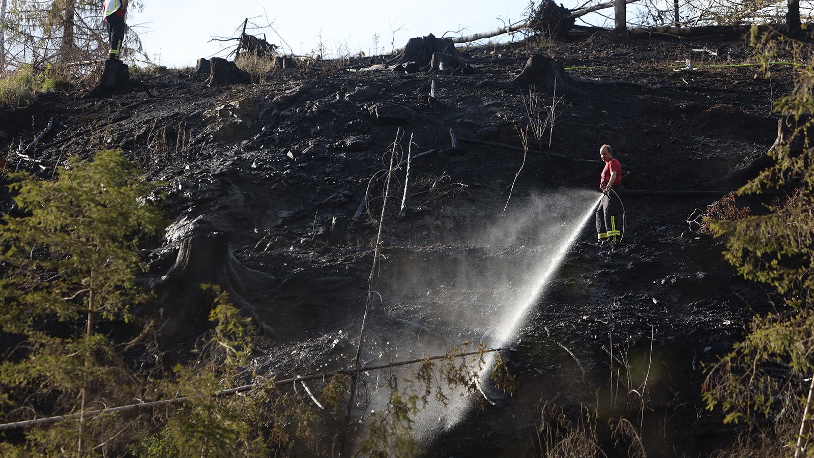 15.05.2022, Sachsen-Anhalt, Stiege: Ein Feuerwehrmann steht an einem abgebrannten&nbsp;Hang und l&ouml;scht einen Waldbrand bei Stiege im Harz. Auf einer Fl&auml;che von 2500 Quadratmetern brannte es. Rund 200 Einsatzkr&auml;fte der Feuerwehr waren im Einsatz. Foto: Matthias Bein/dpa +++ dpa-Bildfunk +++