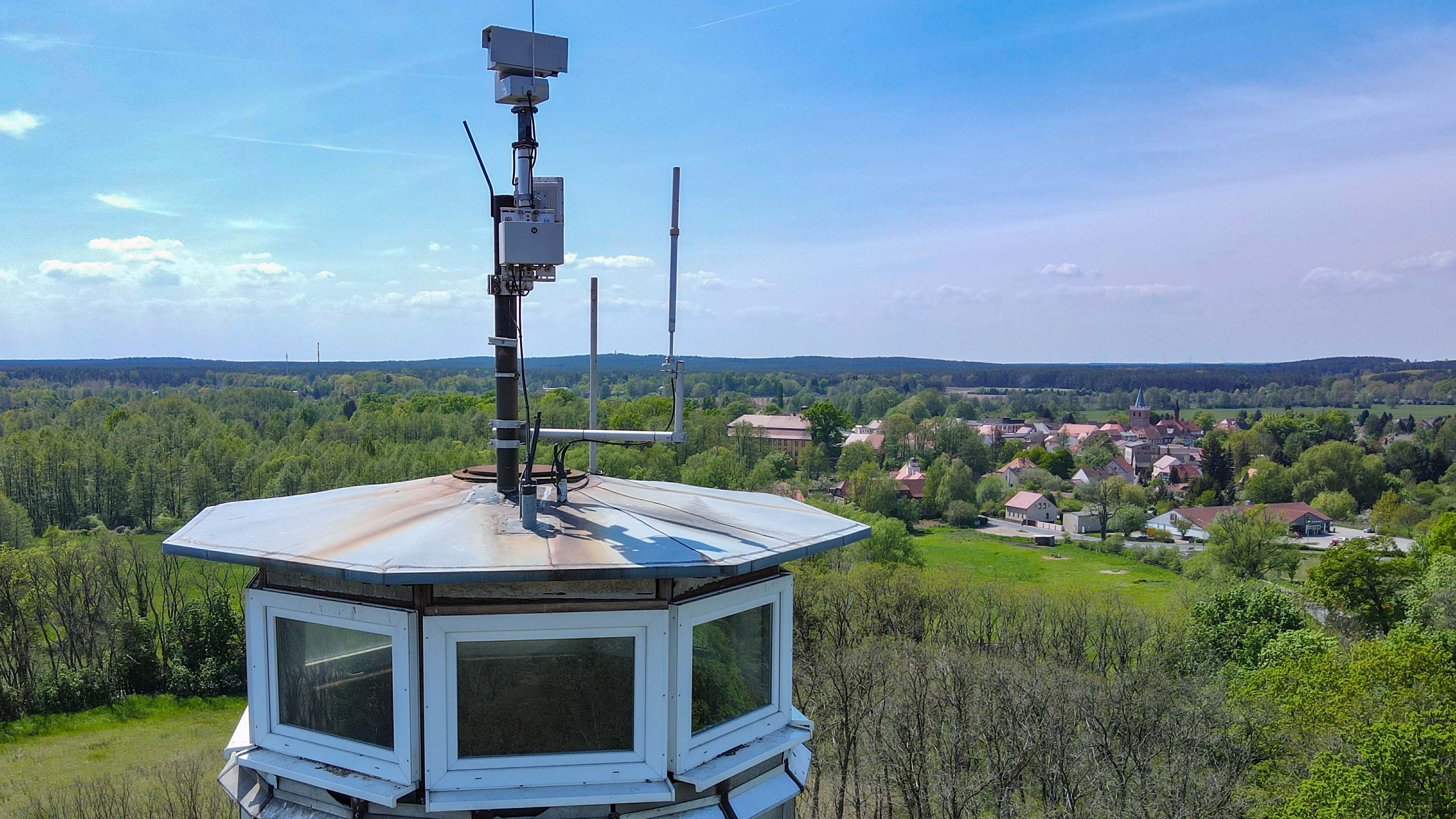 10.05.2022, Brandenburg, Lieberose: Funktechnik sowie eine Kamera sind auf dem Dach eines Feuerwachturmes nahe Lieberose vom Landesbetrieb Forst Brandenburg angebracht (Luftaufnahme mit einer Drohne). Mit den steigenden Temperaturen hat in Brandenburg die Gefahr von Waldbr&permil;nden stark zugenommen. (zu dpa: &acute;&acute;Da ist was&ordf; - Sensoren als scharfes Auge zur Waldbrand&cedil;berwachung&ordf;) Foto: Patrick Pleul/dpa +++ dpa-Bildfunk +++